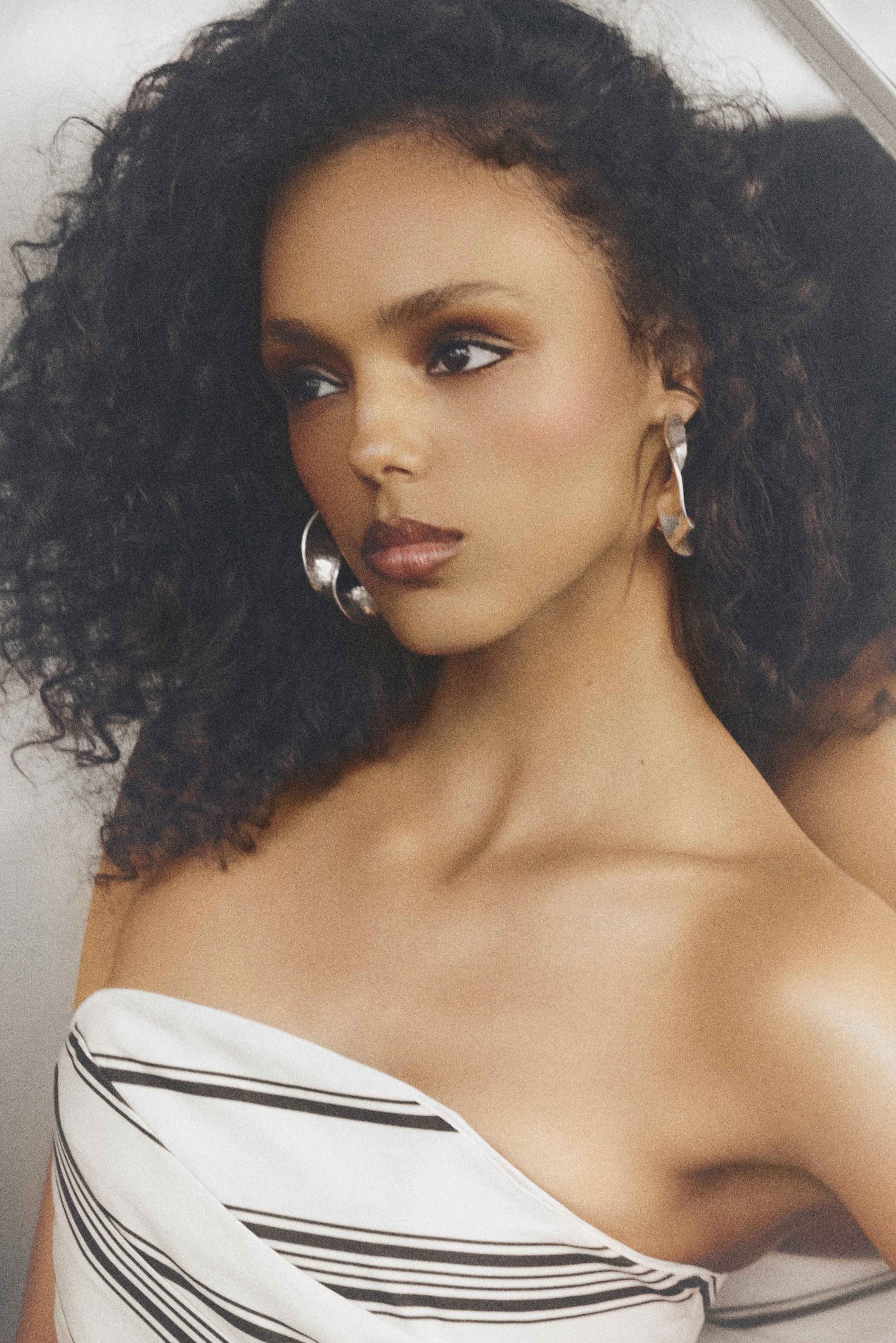 Close-up of a woman with curly hair, silver earrings and a striped strapless gown.