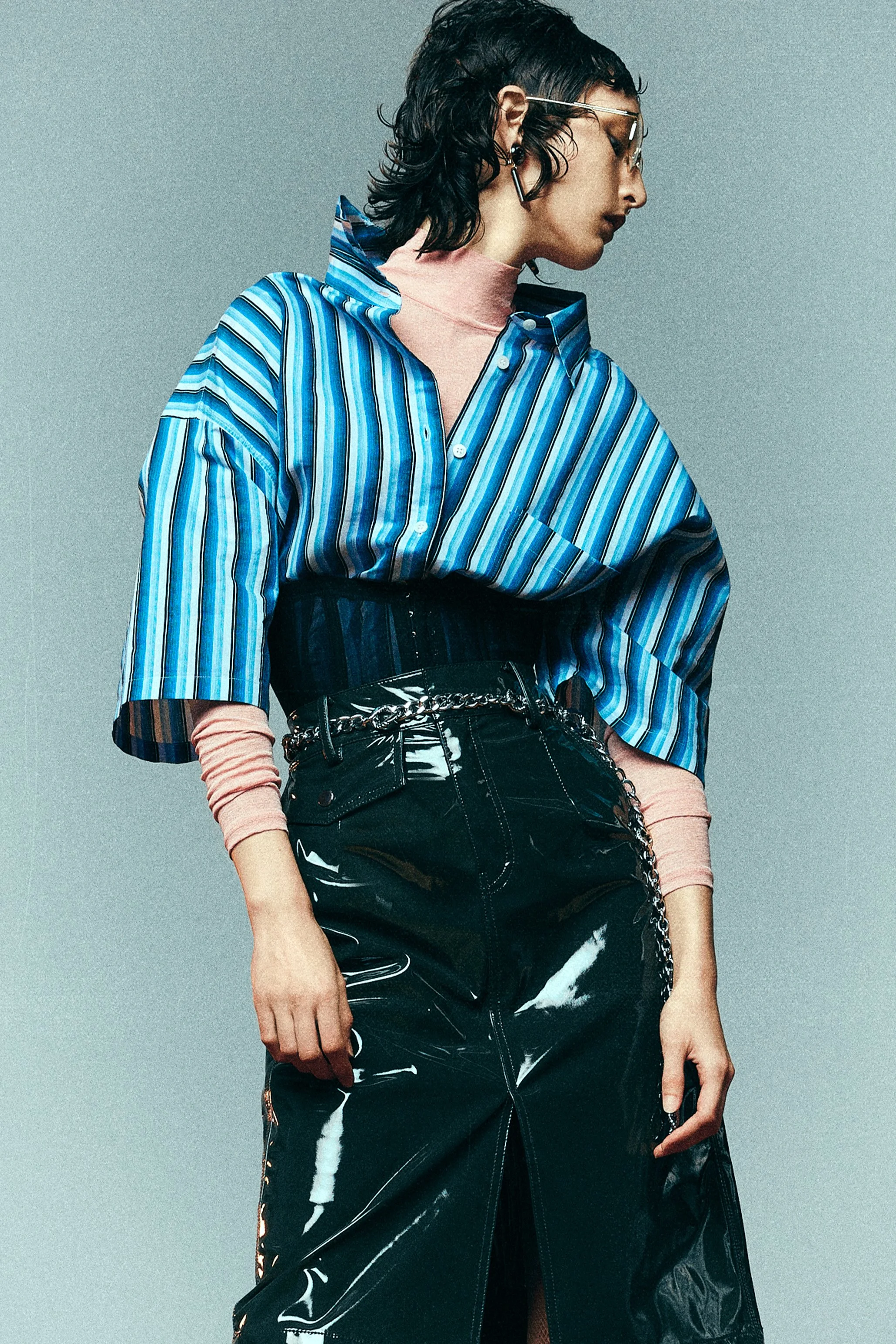 Woman in a blue striped shirt and high-waisted glossy black skirt looking to the side.