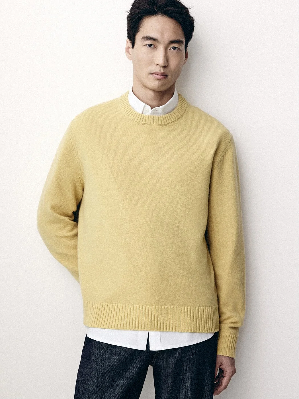 Man wearing a yellow sweater over a white shirt against a pale background.