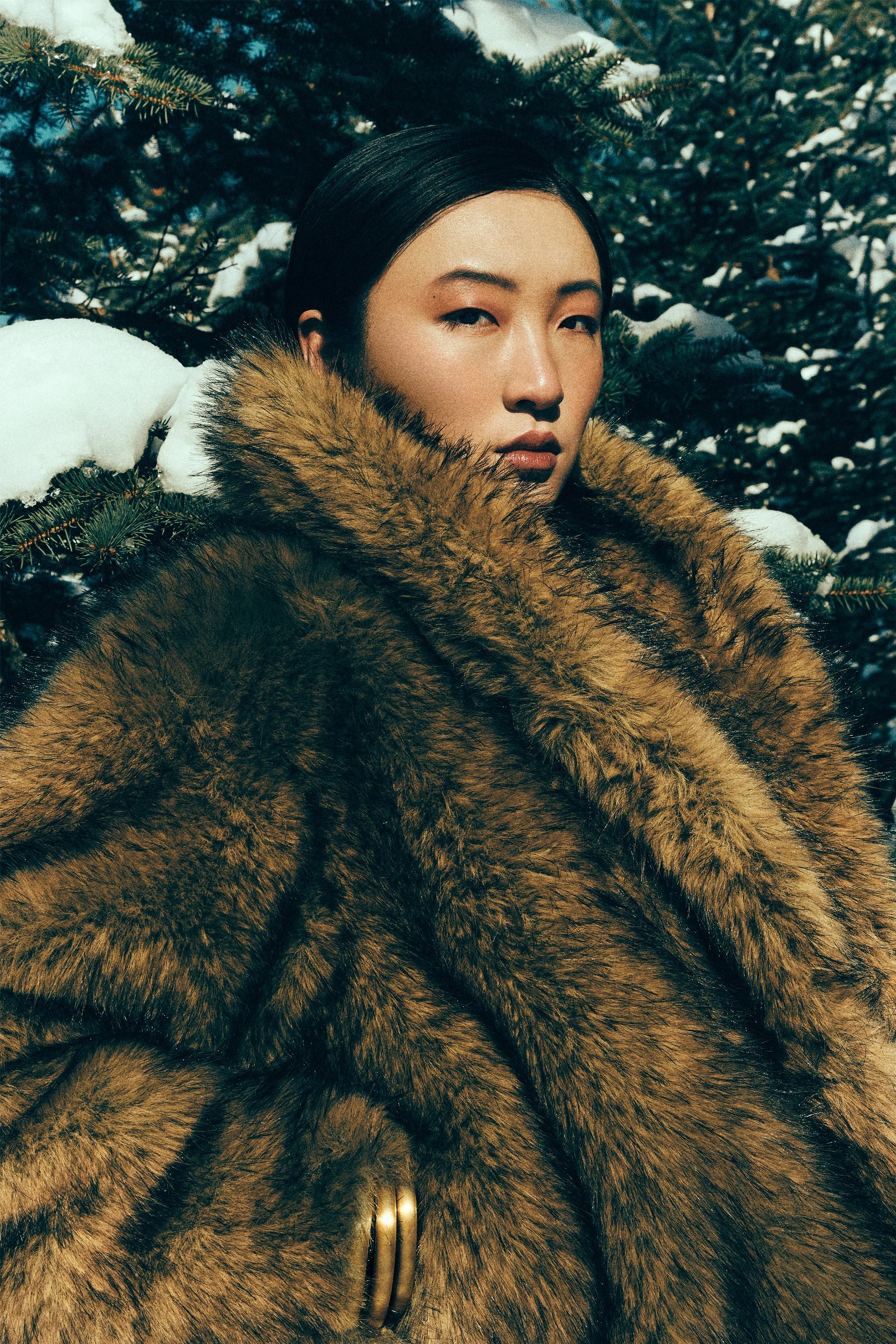 Close portrait of a woman wrapped in a brown fur-textured collar against snowy trees.
