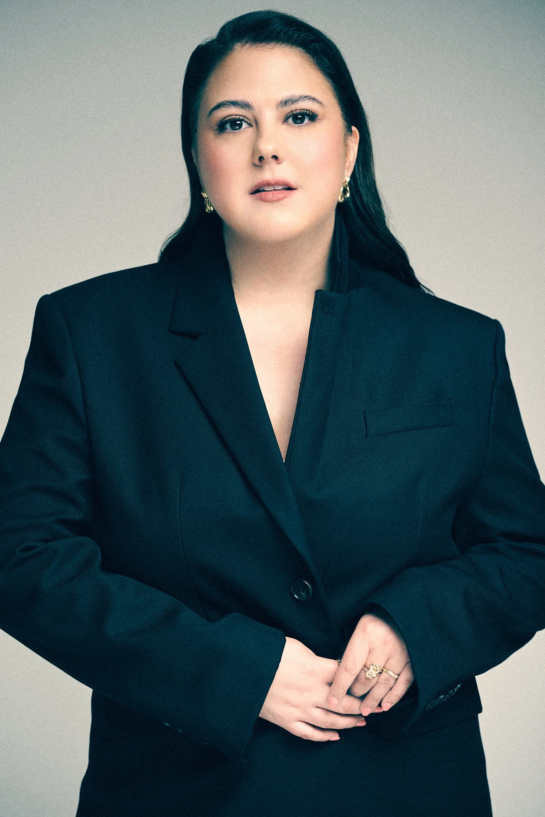 Woman in a black blazer facing the camera with her hands folded at her waist.