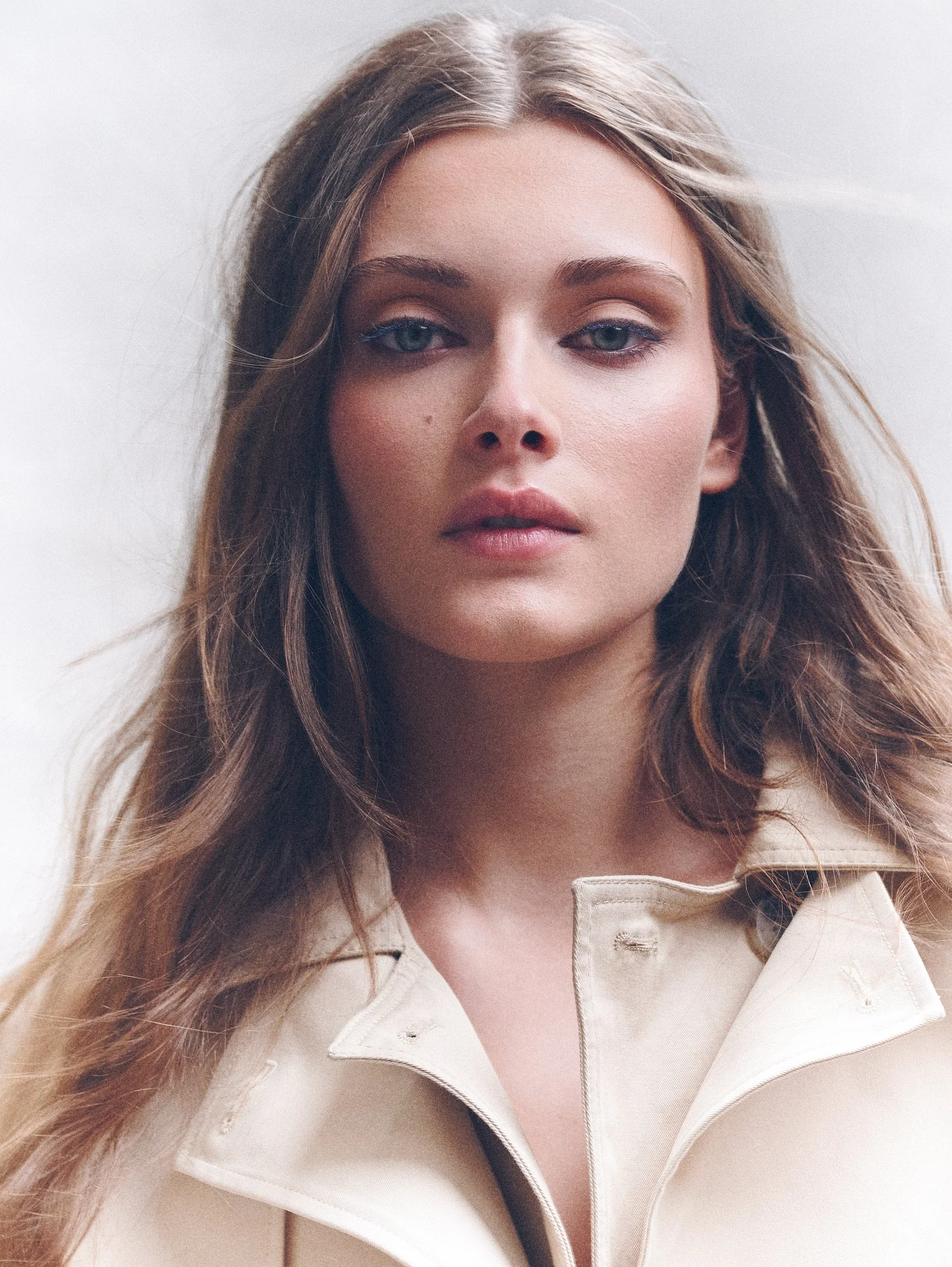 Close portrait of a woman with long loose hair wearing a cream collared coat.