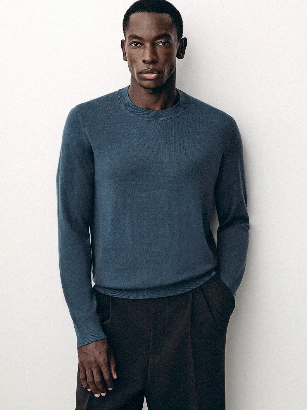 Man facing the camera in a muted blue crew-neck sweater.