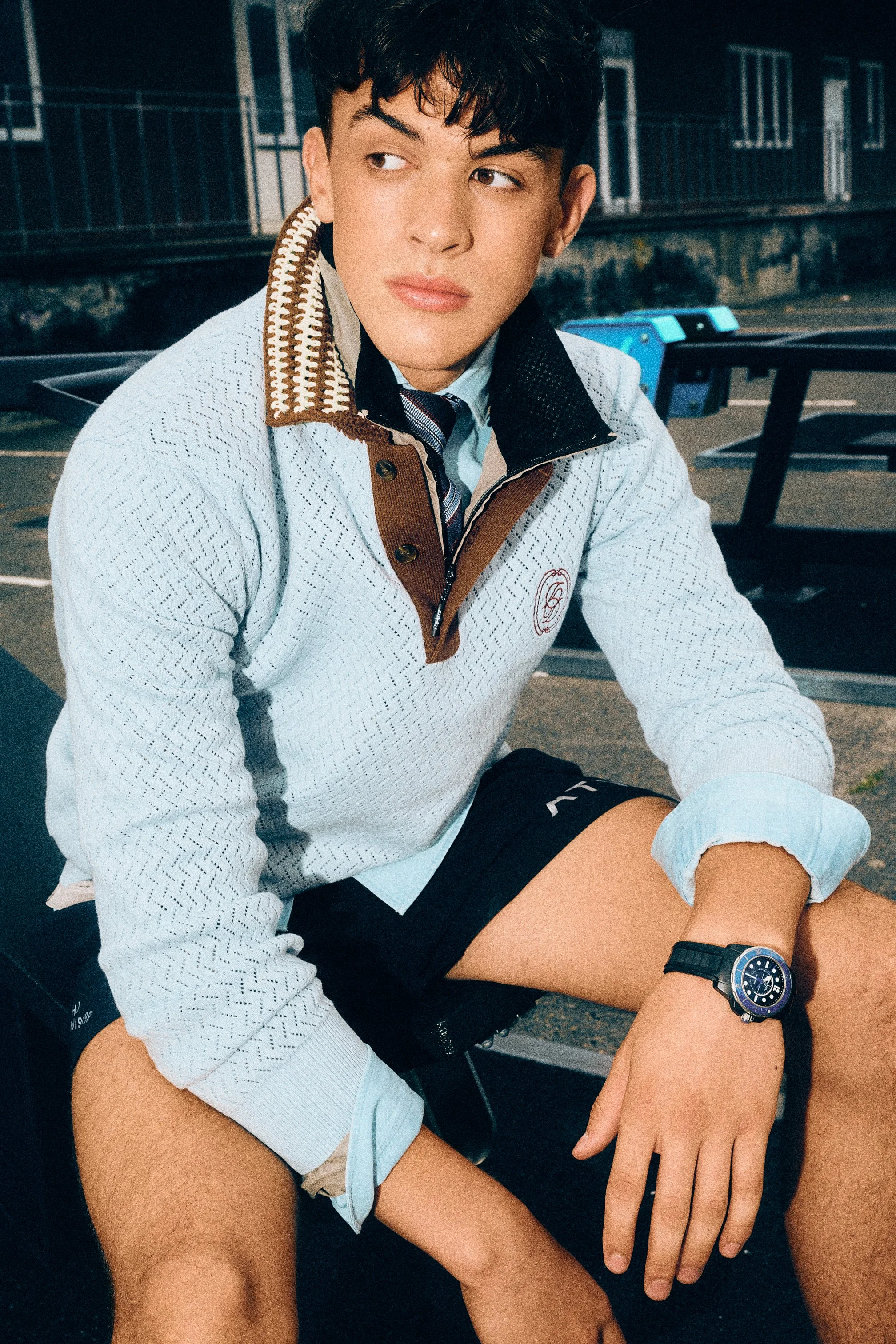 Close portrait of a man in a pale blue knit top seated on outdoor exercise equipment.