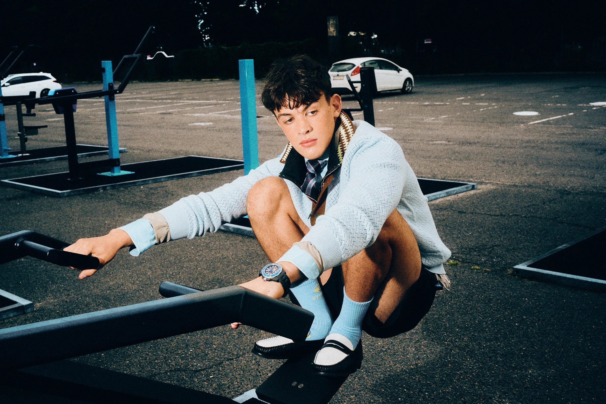 Man crouching on outdoor exercise equipment in a pale blue top and dark shorts.