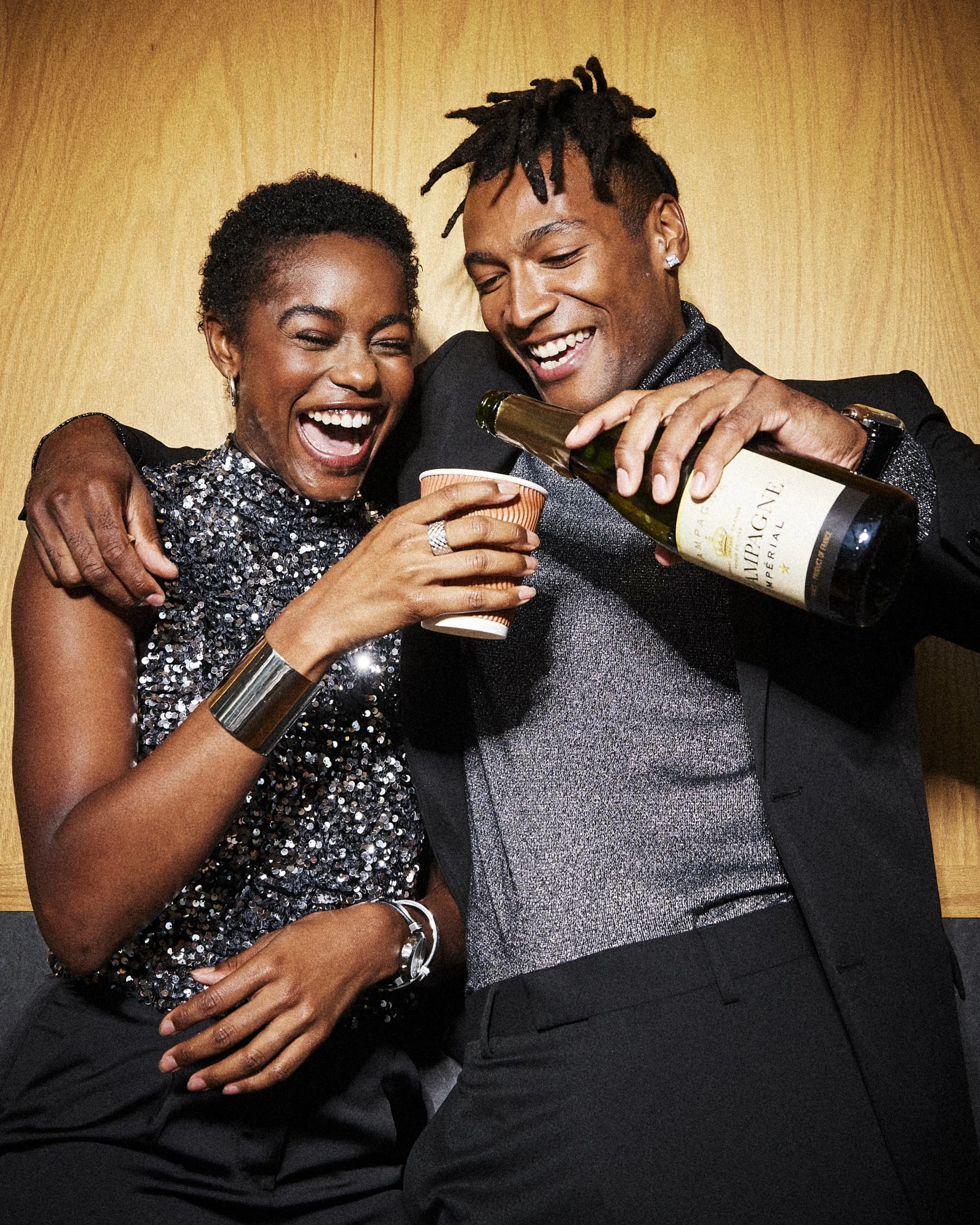 Two laughing party guests, one pouring a drink while the other holds a cup.