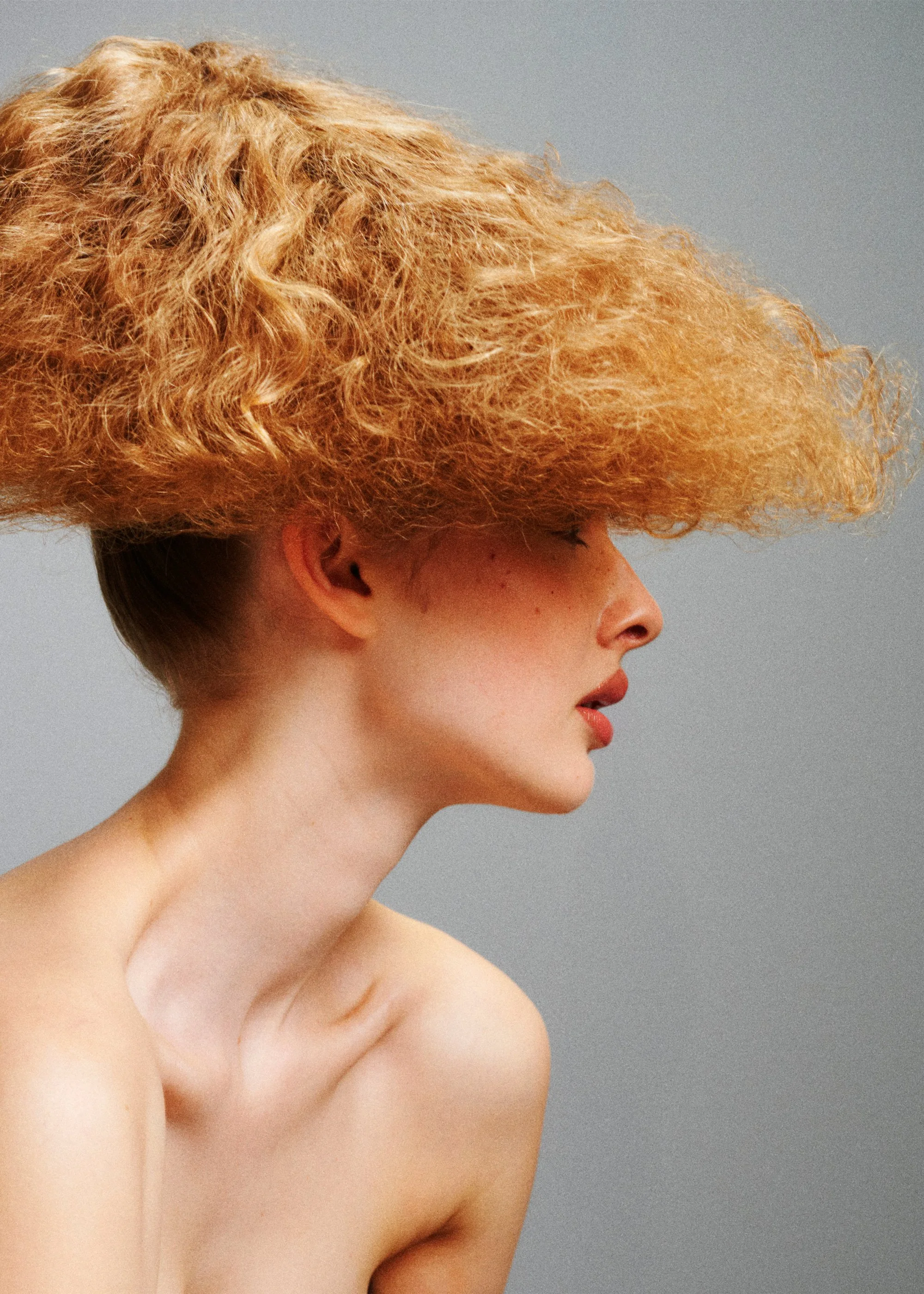 Side-profile beauty portrait with voluminous curly blonde hair shaped into a broad horizontal silhouette.