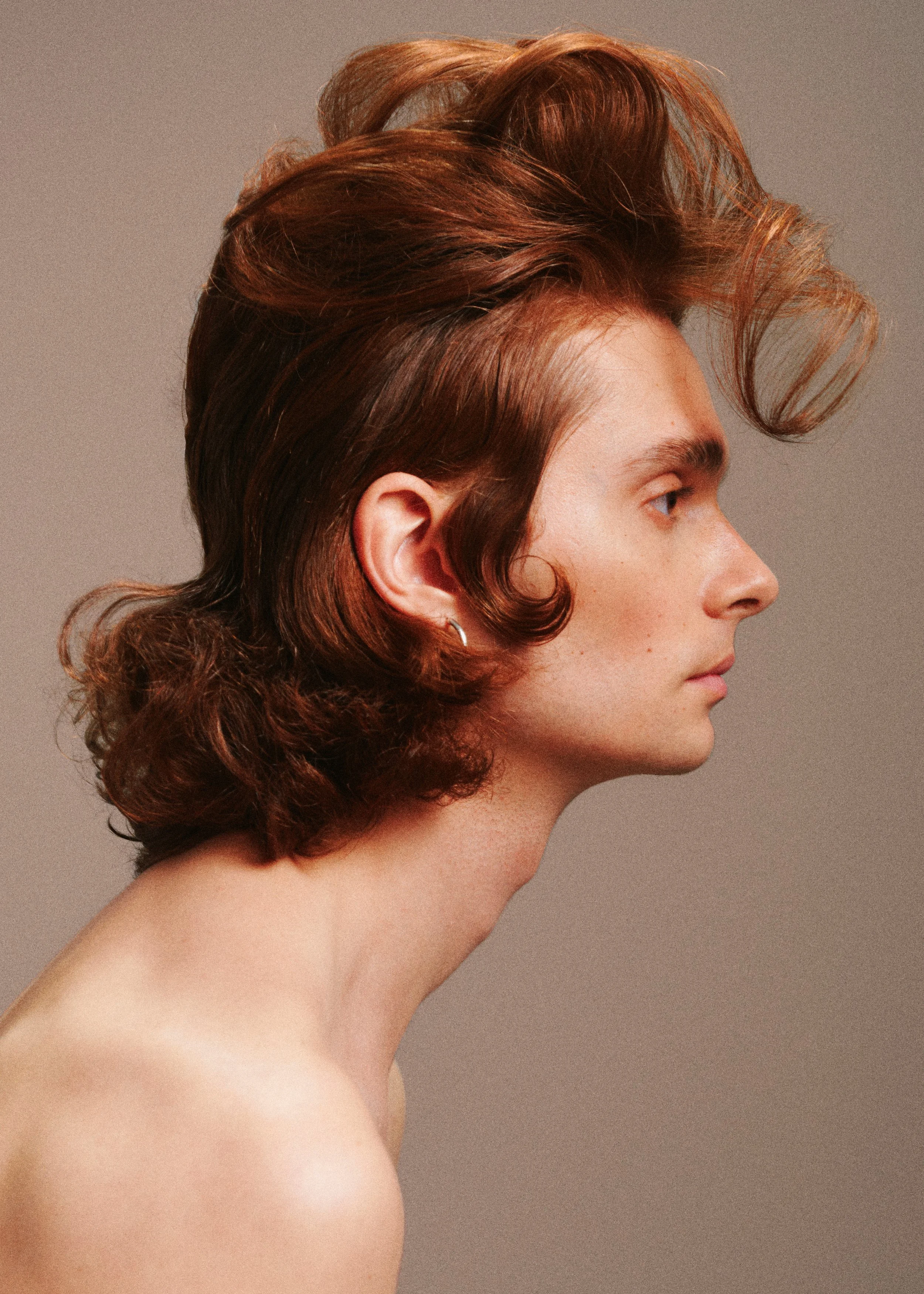 Side-profile beauty portrait with sculpted auburn curls swept into a high, rounded hairstyle.