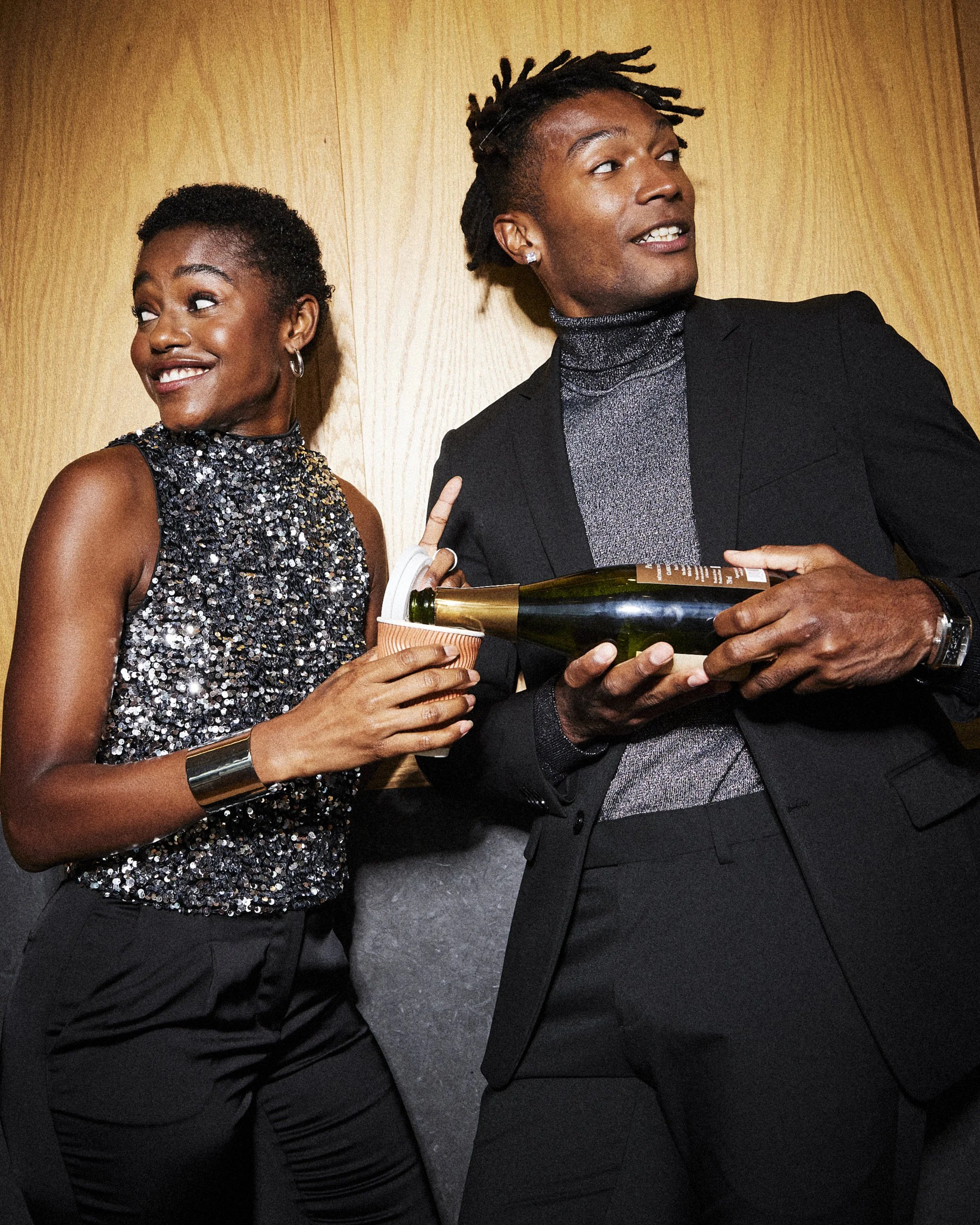 Two party guests looking to the side while holding a bottle and a cup.