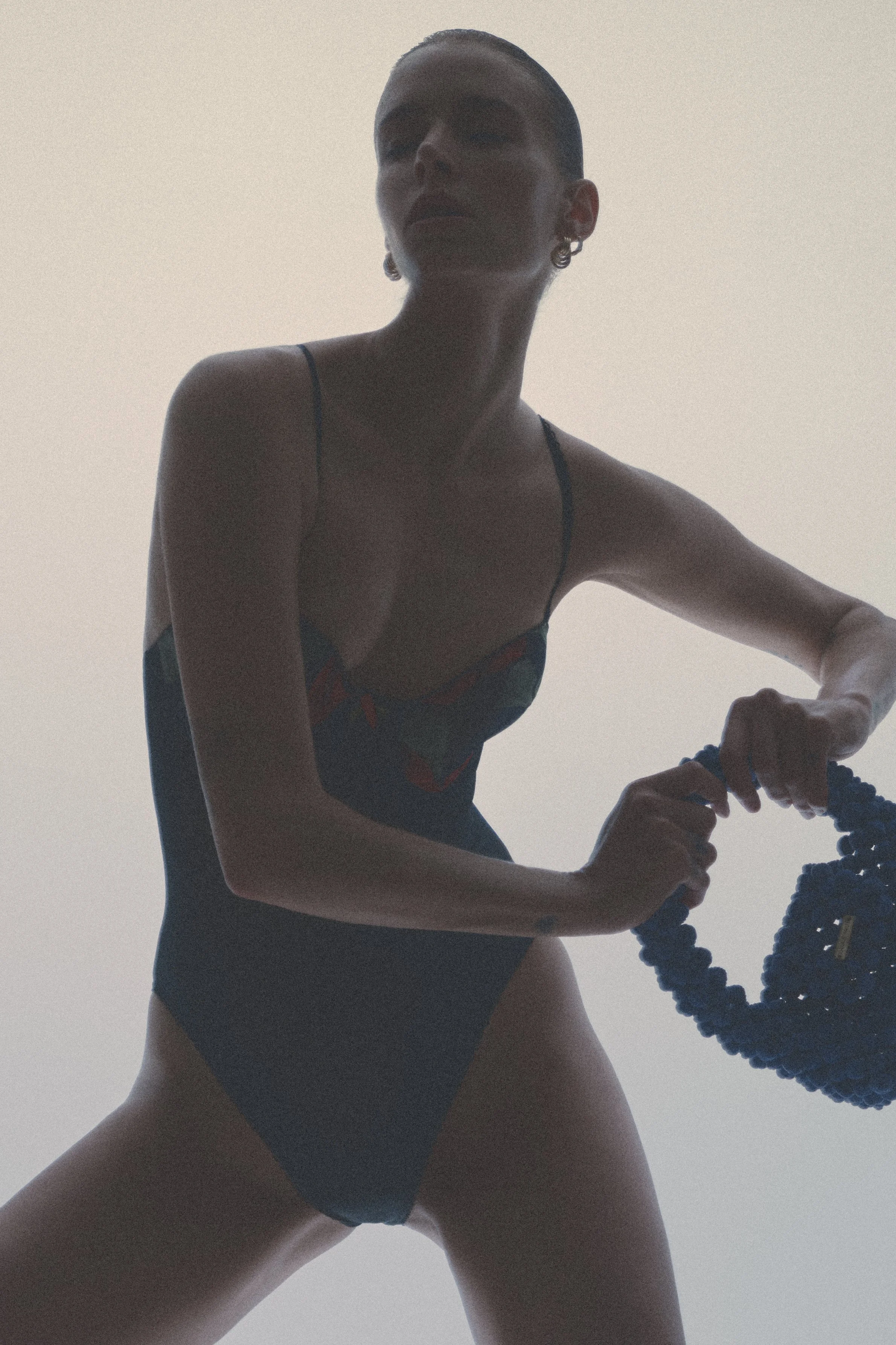 Closer backlit portrait of a woman in black lingerie holding a small beaded handbag.