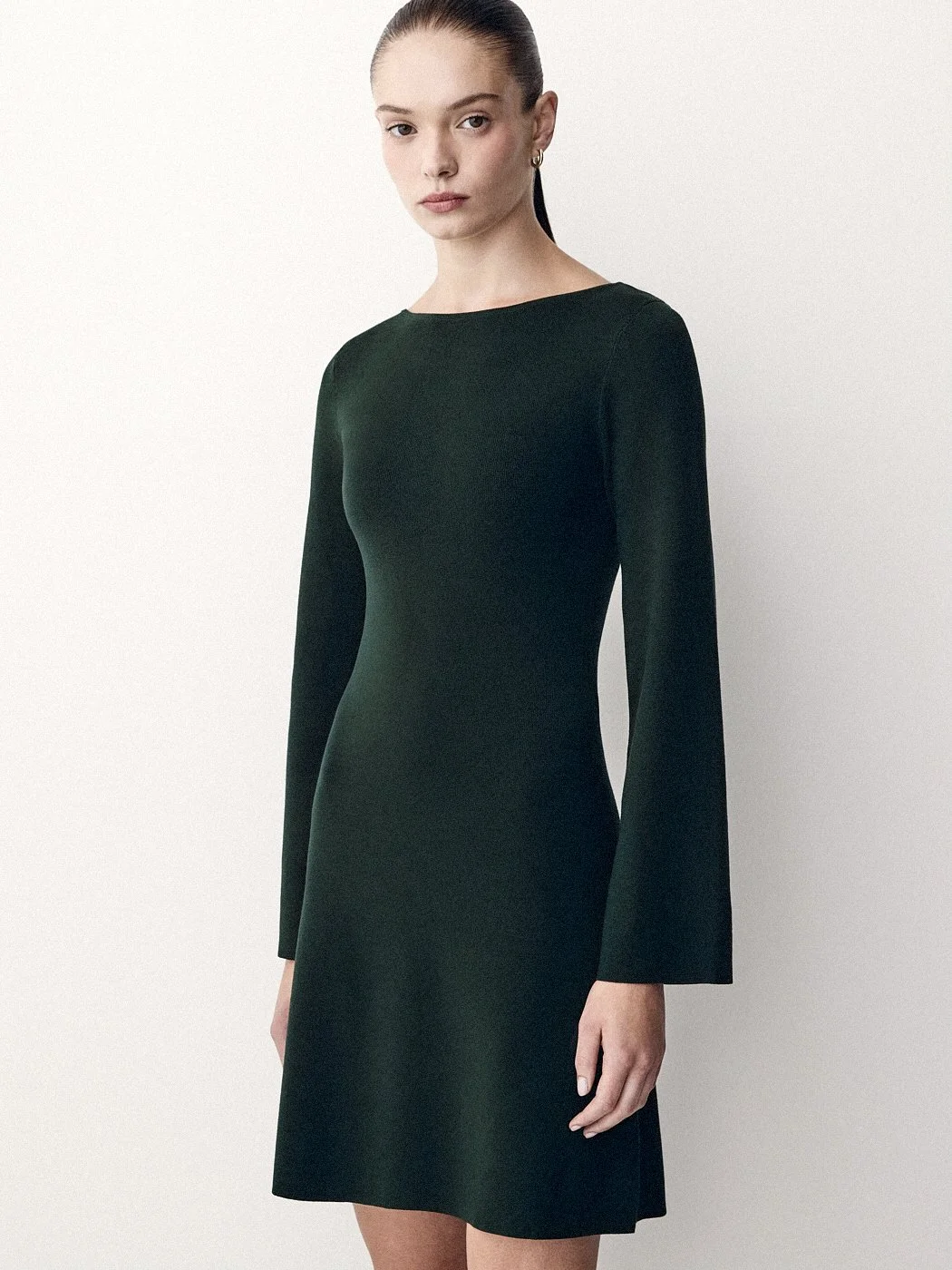 Woman in a long-sleeved dark green dress against an off-white background.