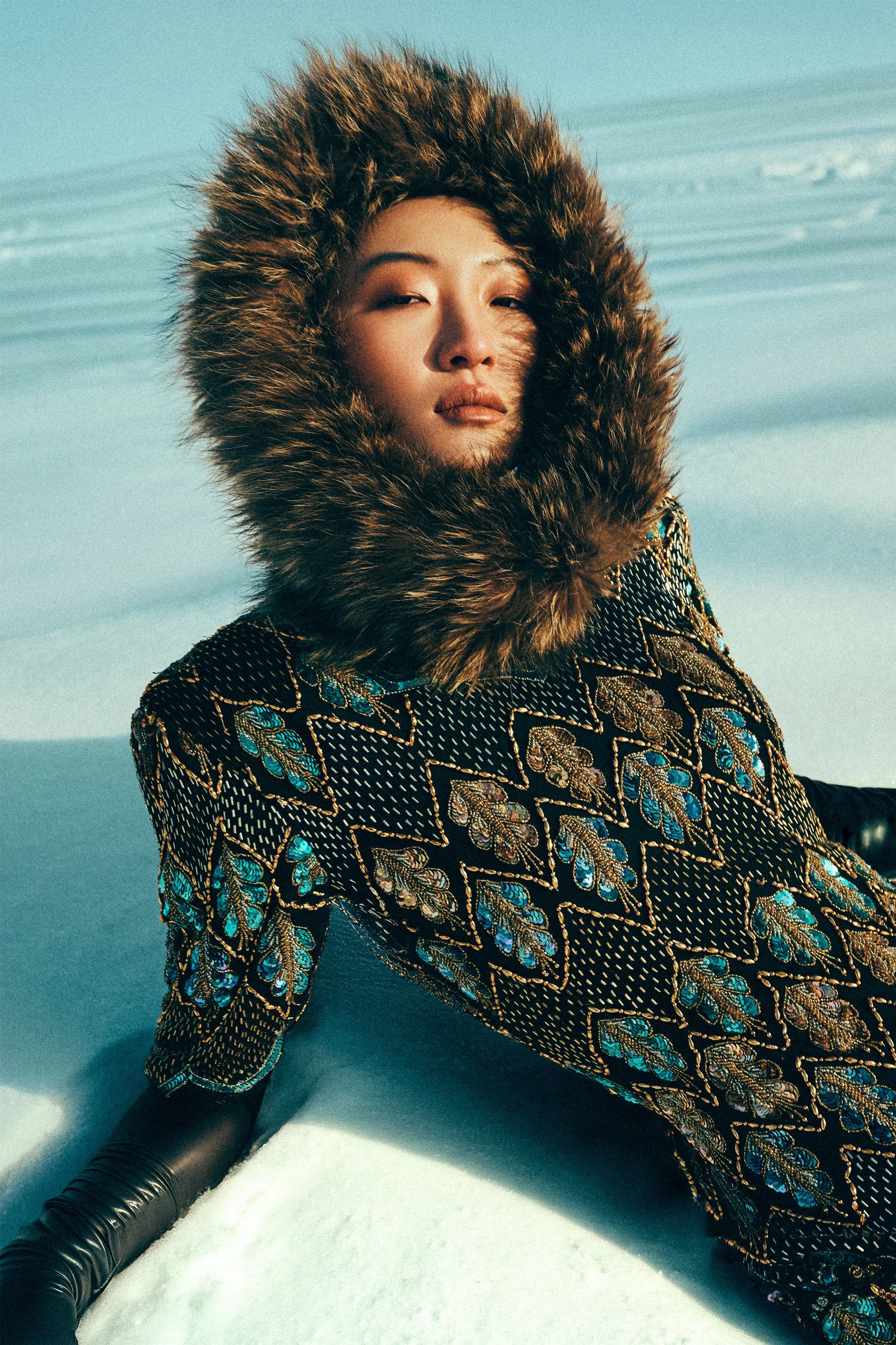 Woman reclining in snow wearing a patterned coat with a fur-trimmed hood.