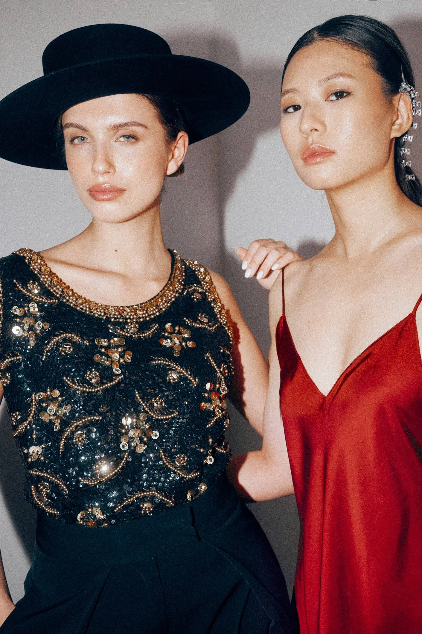 Two women posing together in a black embellished top and a red satin dress.