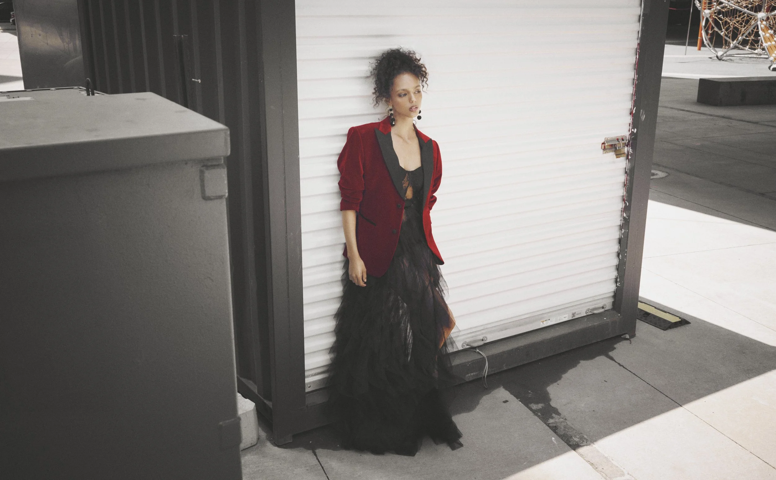 Woman in a burgundy jacket and long black skirt beside an industrial doorway.