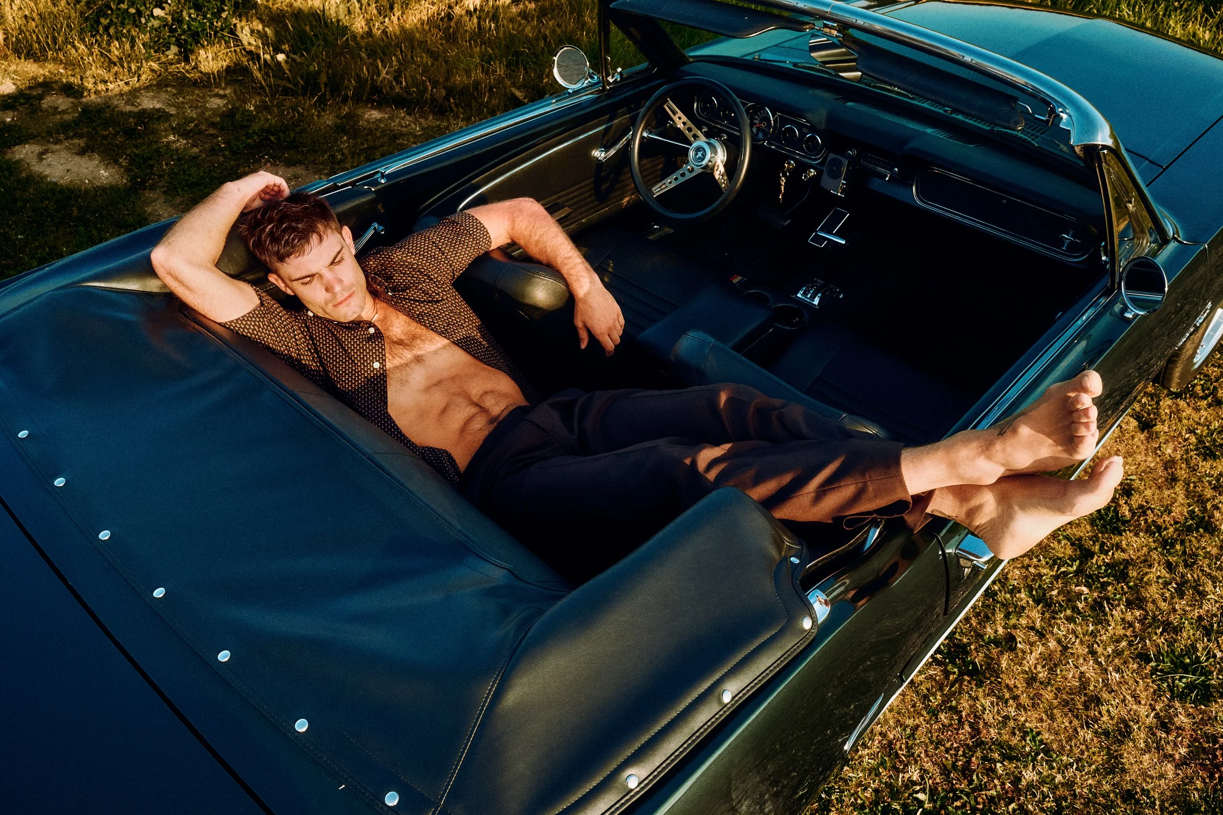 Overhead view of a man reclining across the seats of a turquoise convertible.