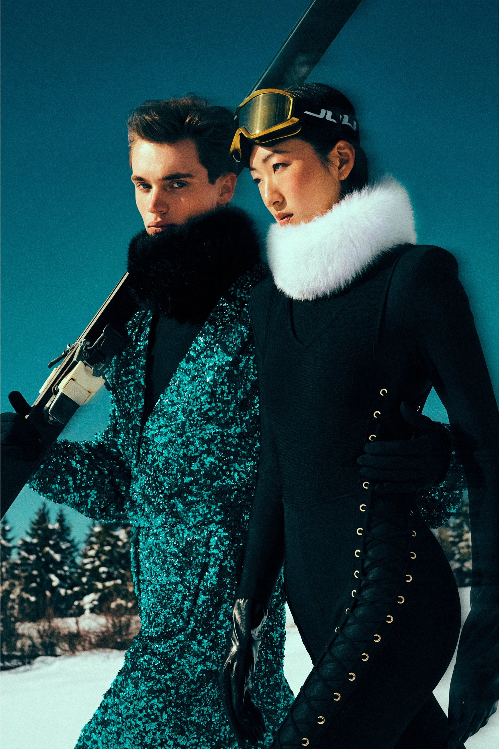Two models in winter clothing standing together with skis against a deep blue sky.