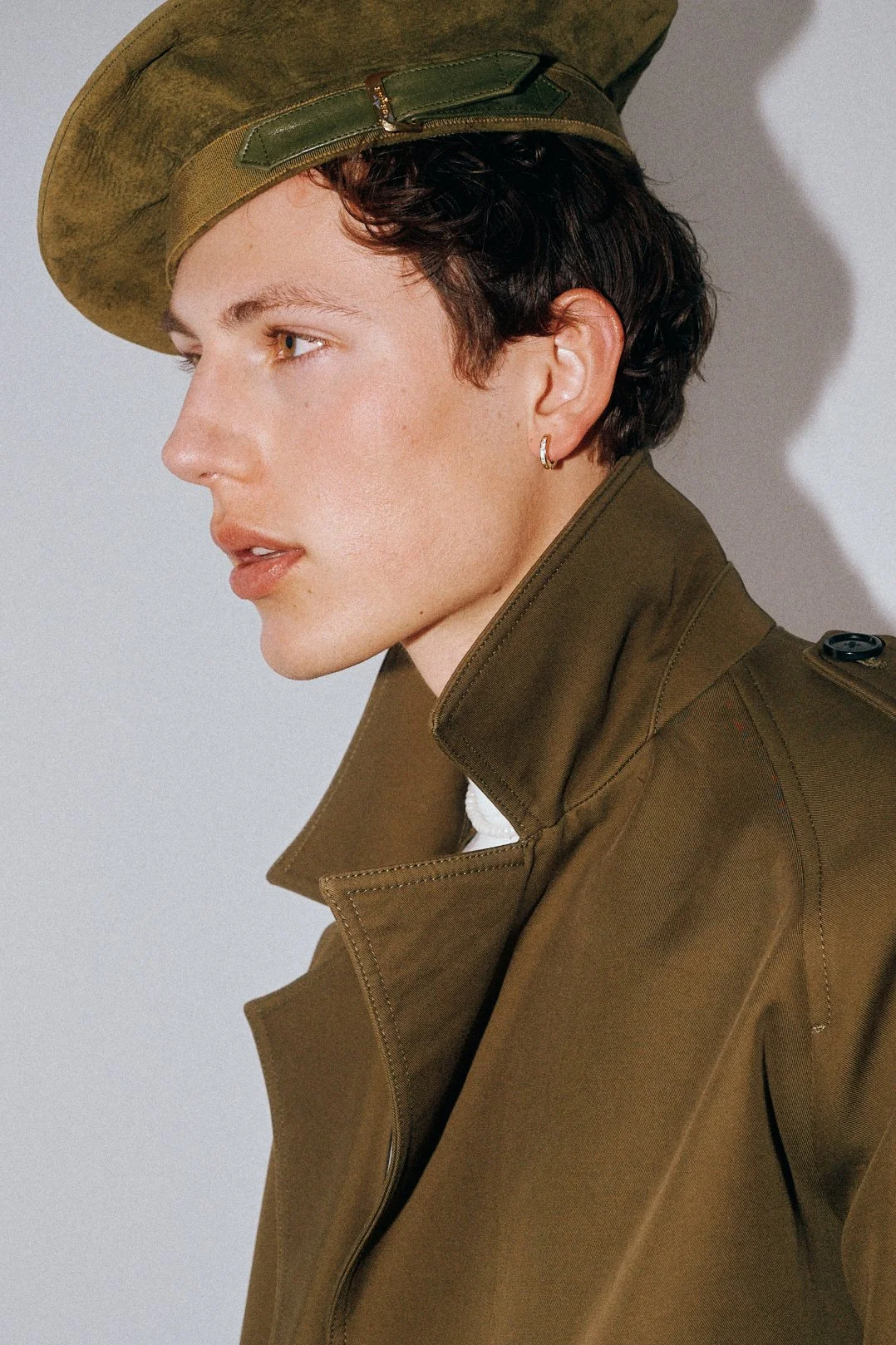 Side-profile portrait of a man in an olive coat and green beret.