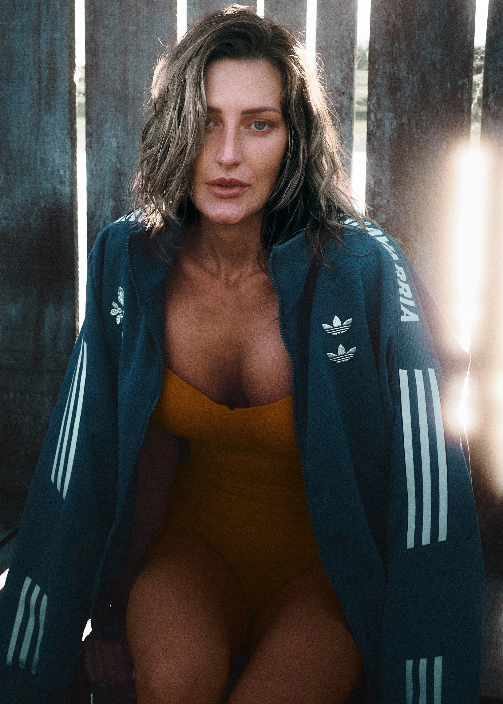 Woman in a dark track jacket over a yellow swimsuit inside a wooden waterfront structure.