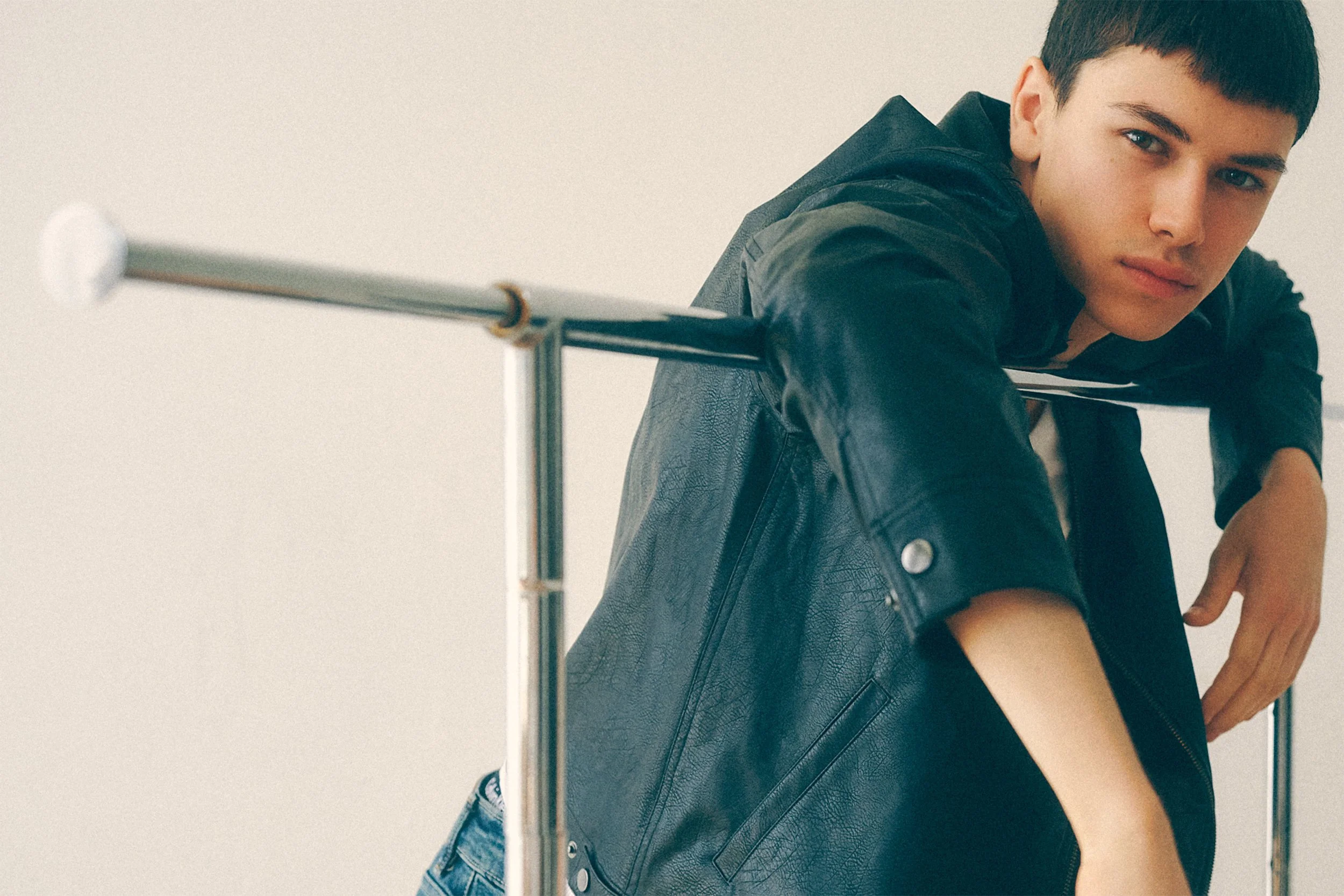 Young man in a black jacket leaning across the back of a metal chair.