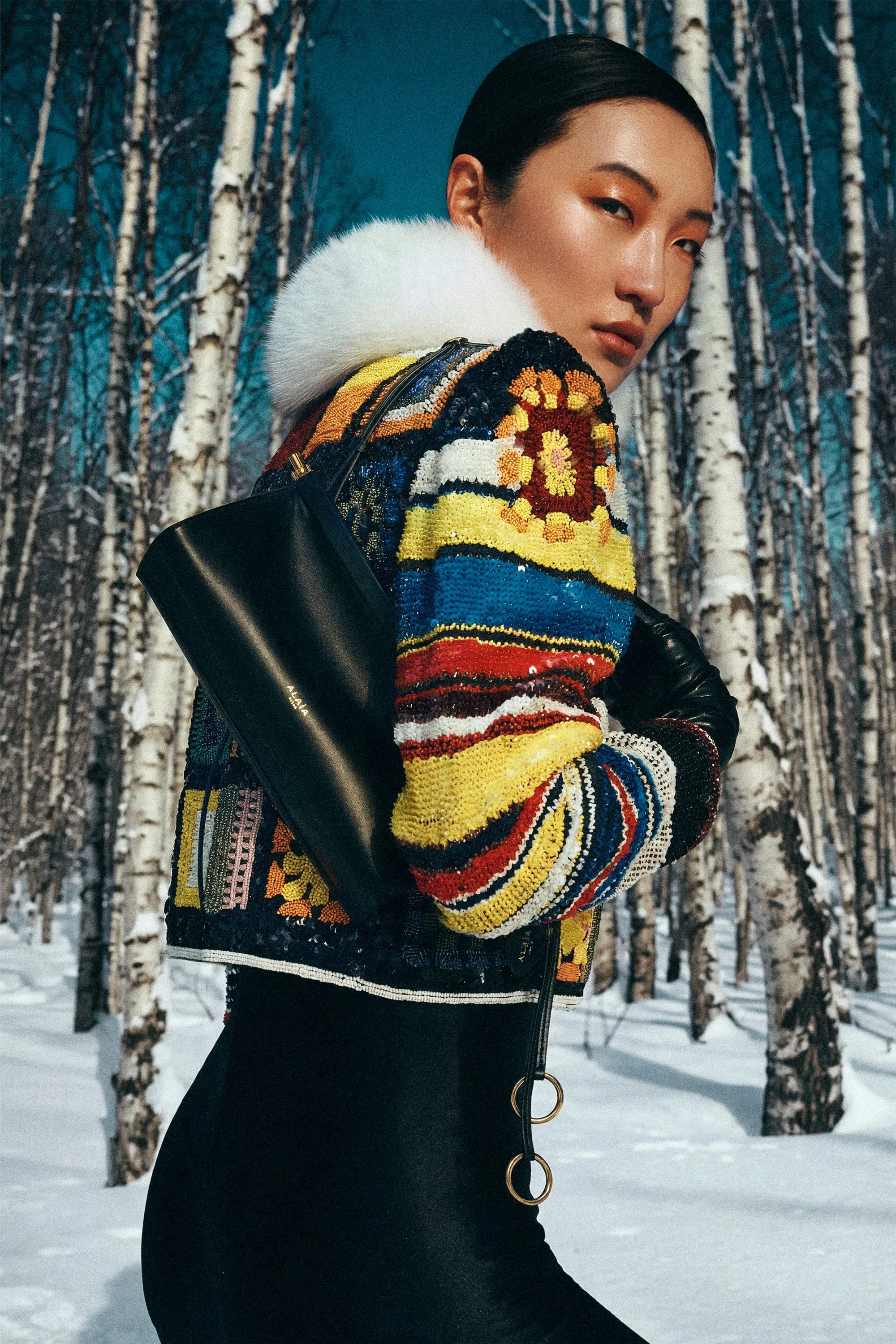 Woman looking over her shoulder in colourful knitwear among snow-covered birch trees.