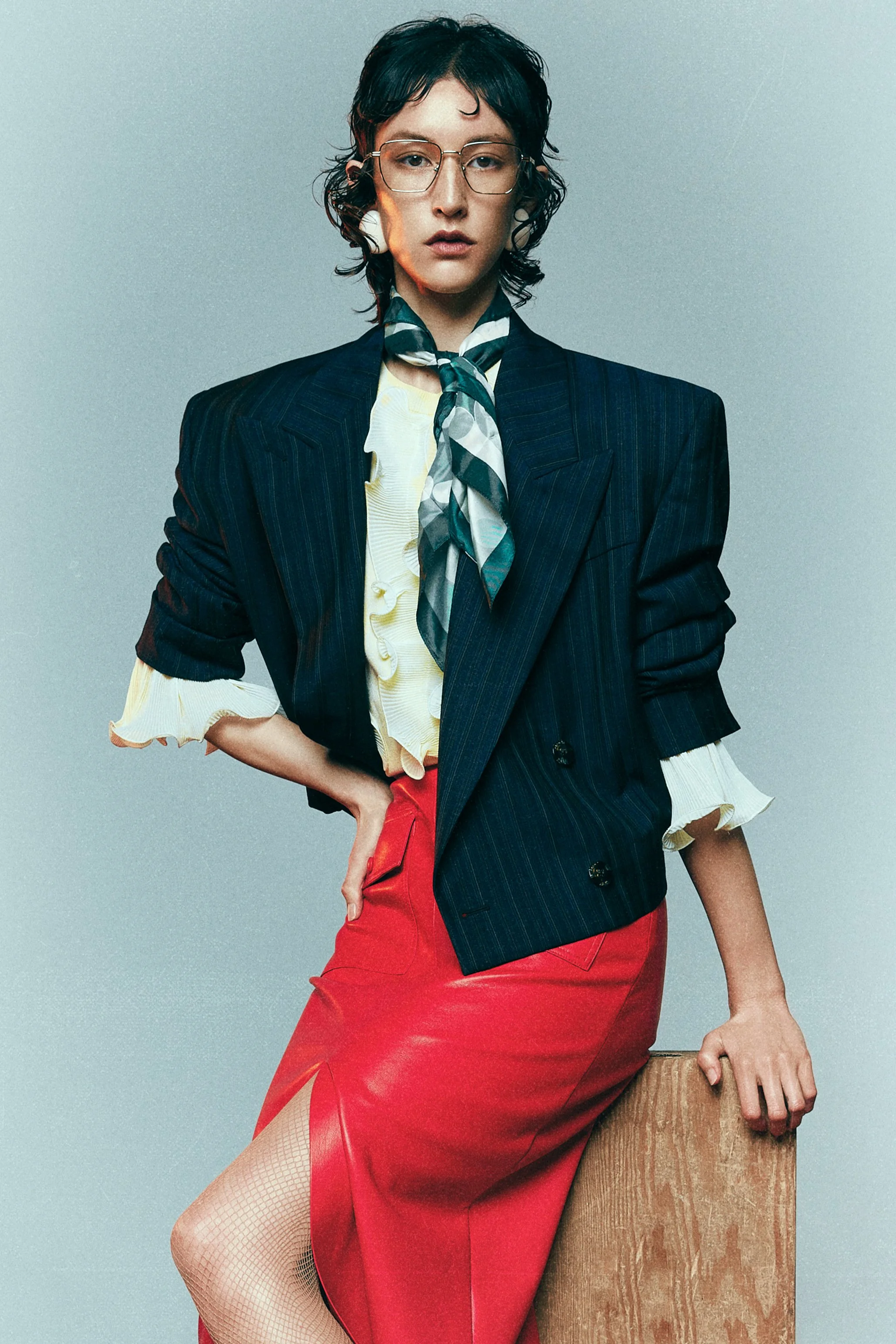 Woman in a navy blazer, printed neck scarf and red skirt standing beside a wooden block.