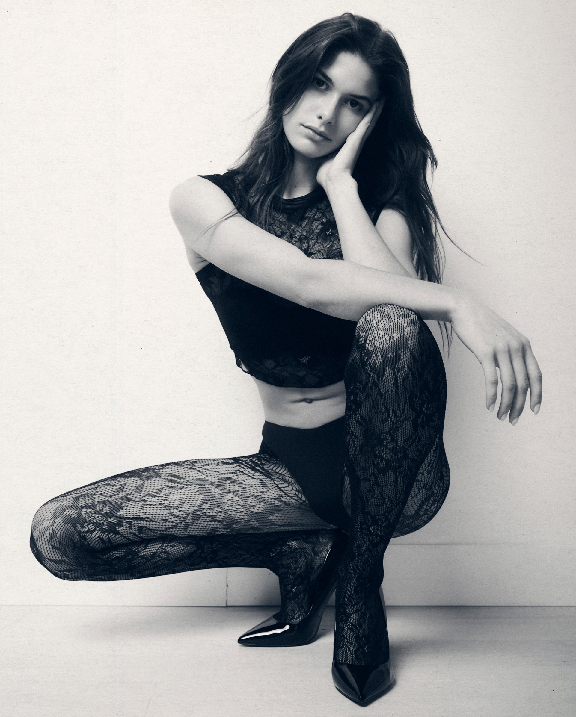 Black-and-white portrait of a woman crouching in a black crop top and lace trousers.