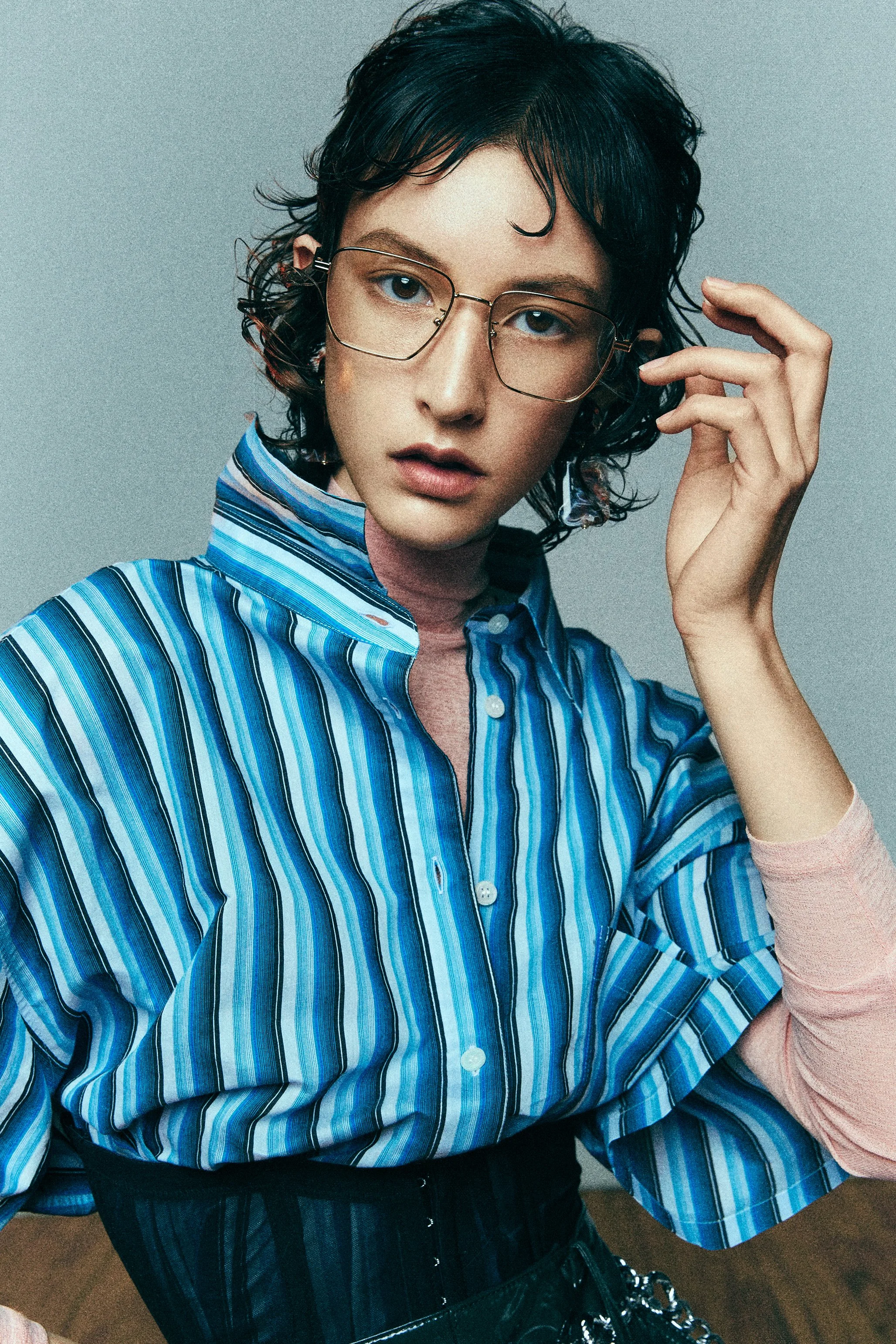 Close portrait of a woman in a blue striped shirt adjusting her glasses.