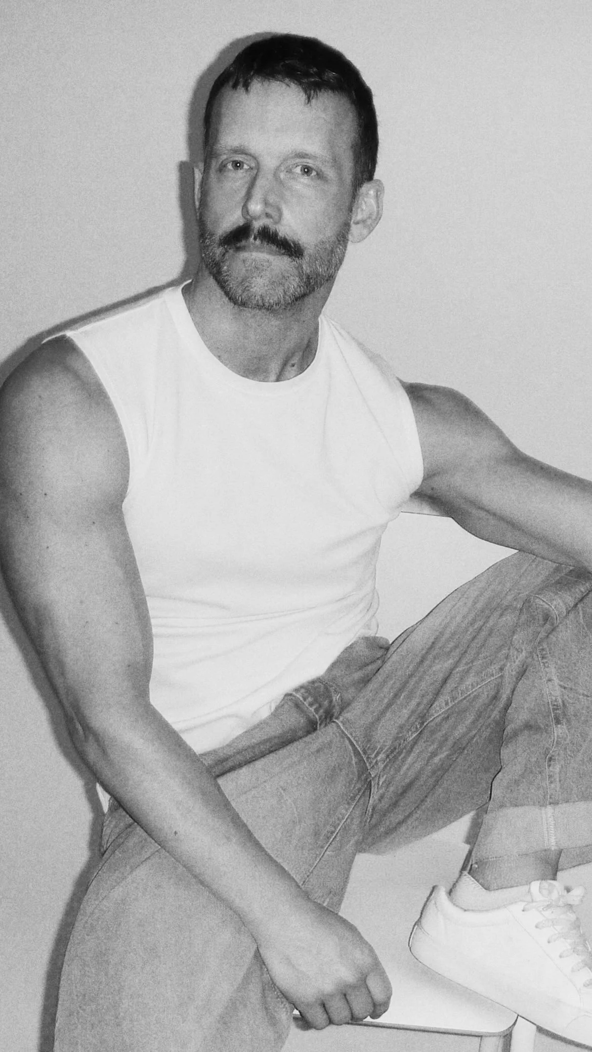 Black-and-white portrait of photographer Johan Magnus seated in a white sleeveless top, jeans and white shoes.