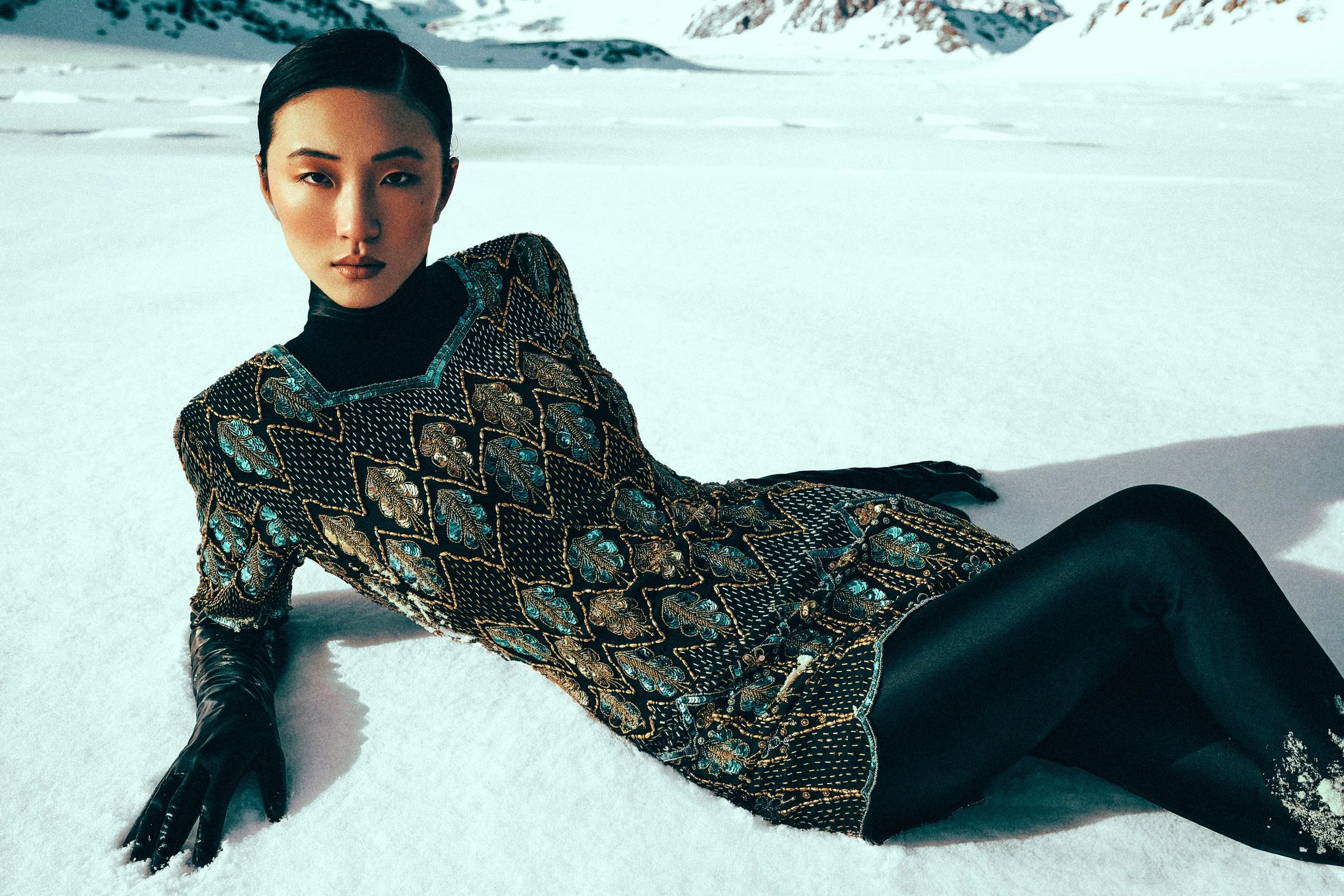 Woman in a patterned dress and black gloves reclining on a snowy slope.