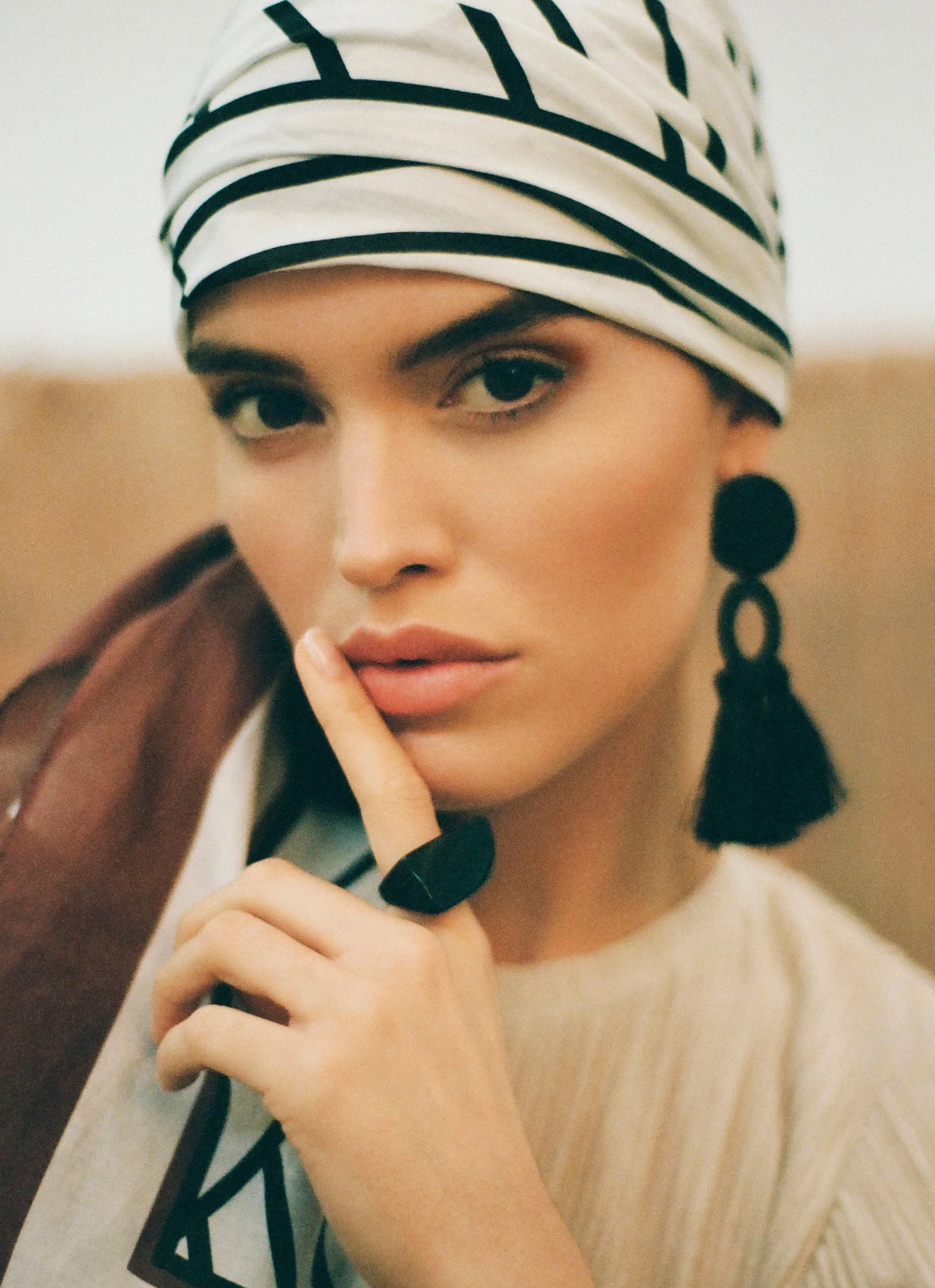 Close beauty portrait of a woman in a patterned head wrap and black geometric earrings.