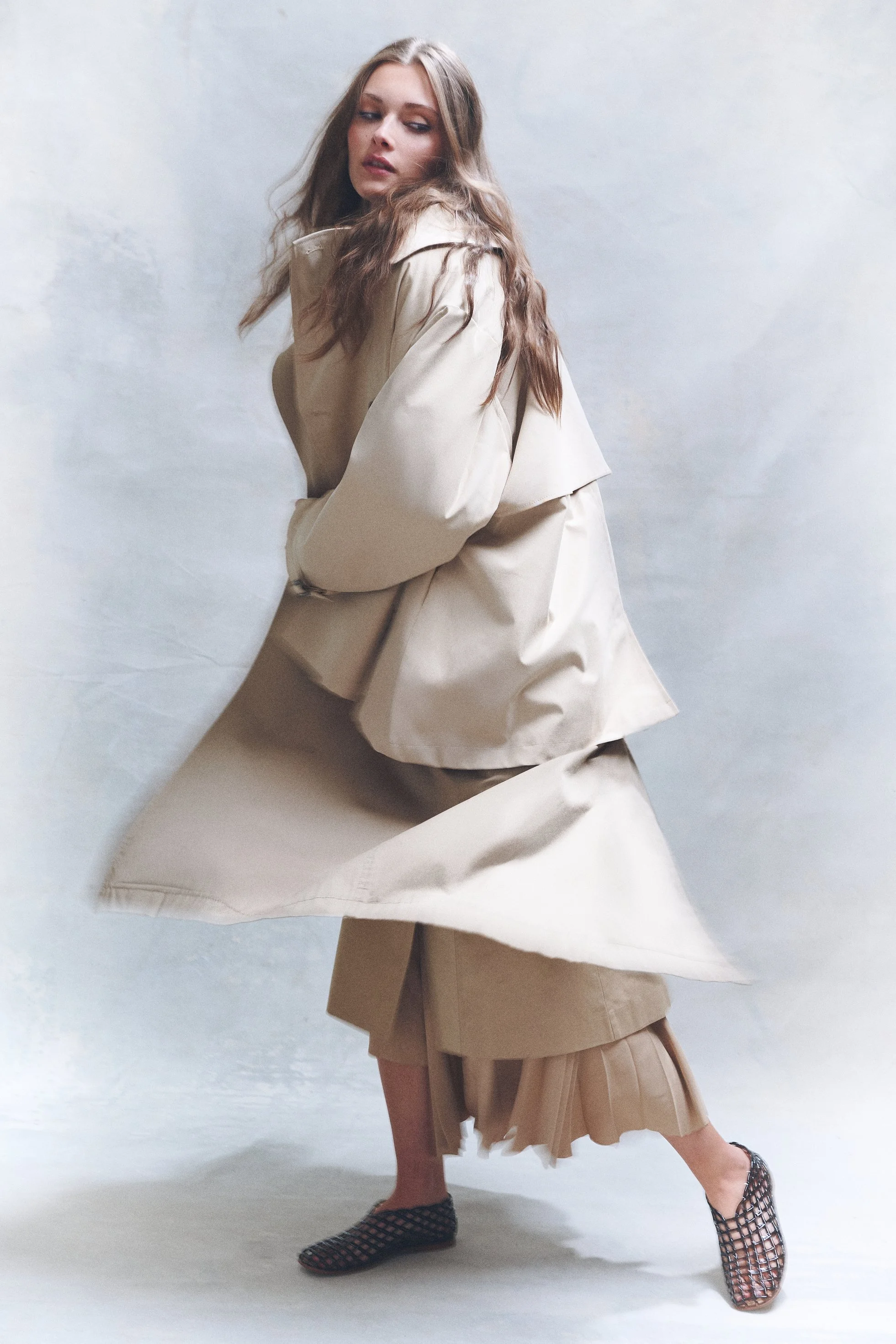 Woman turning in a layered cream coat as the fabric swings around her.