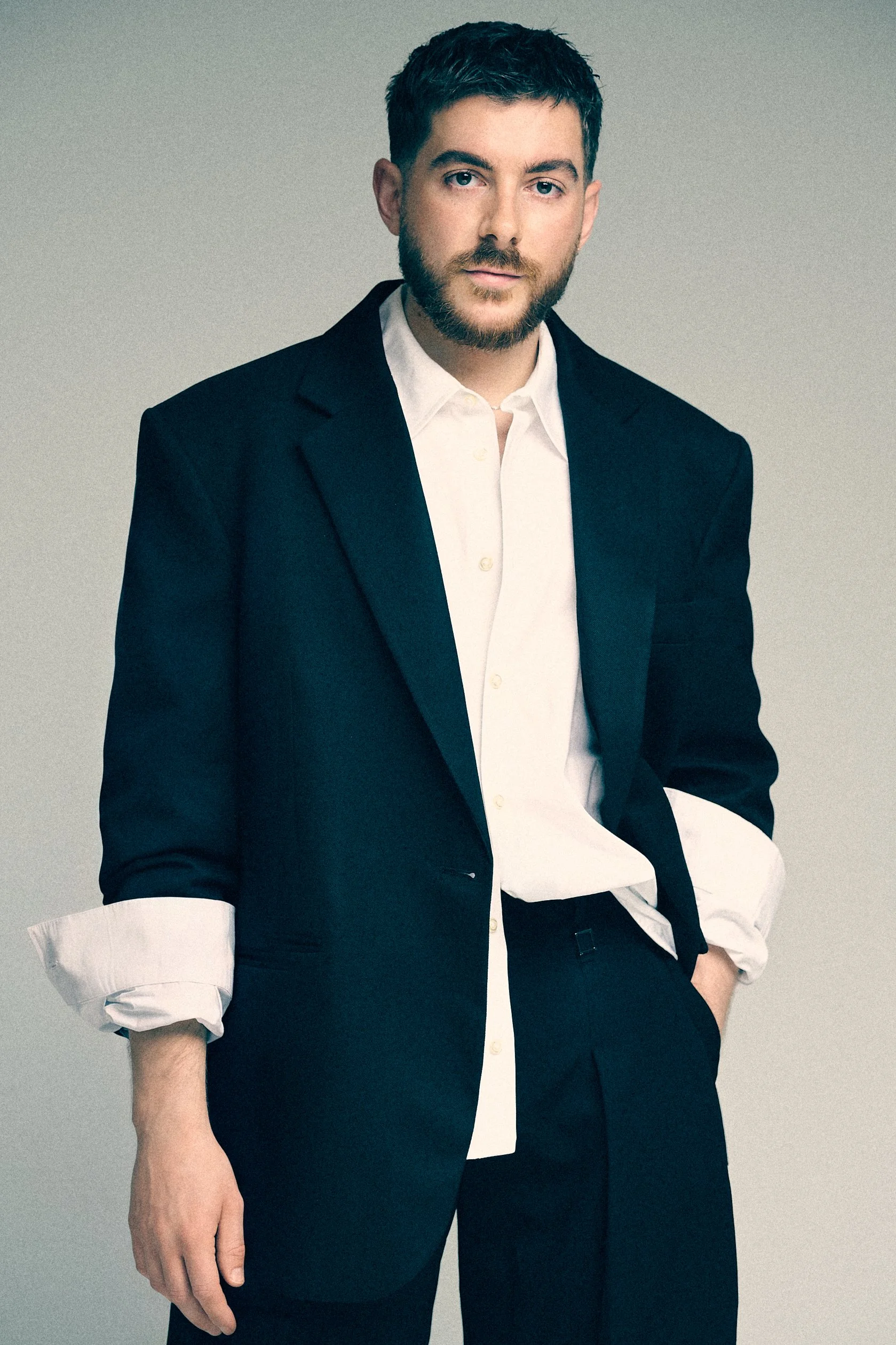 Man wearing a black blazer over a white shirt with rolled cuffs.
