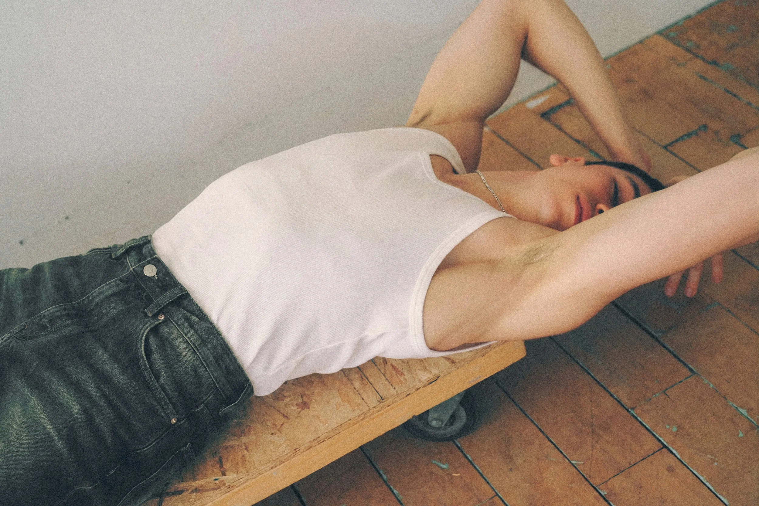 Overhead view of a young man lying on a wooden bench with his arms above his head.