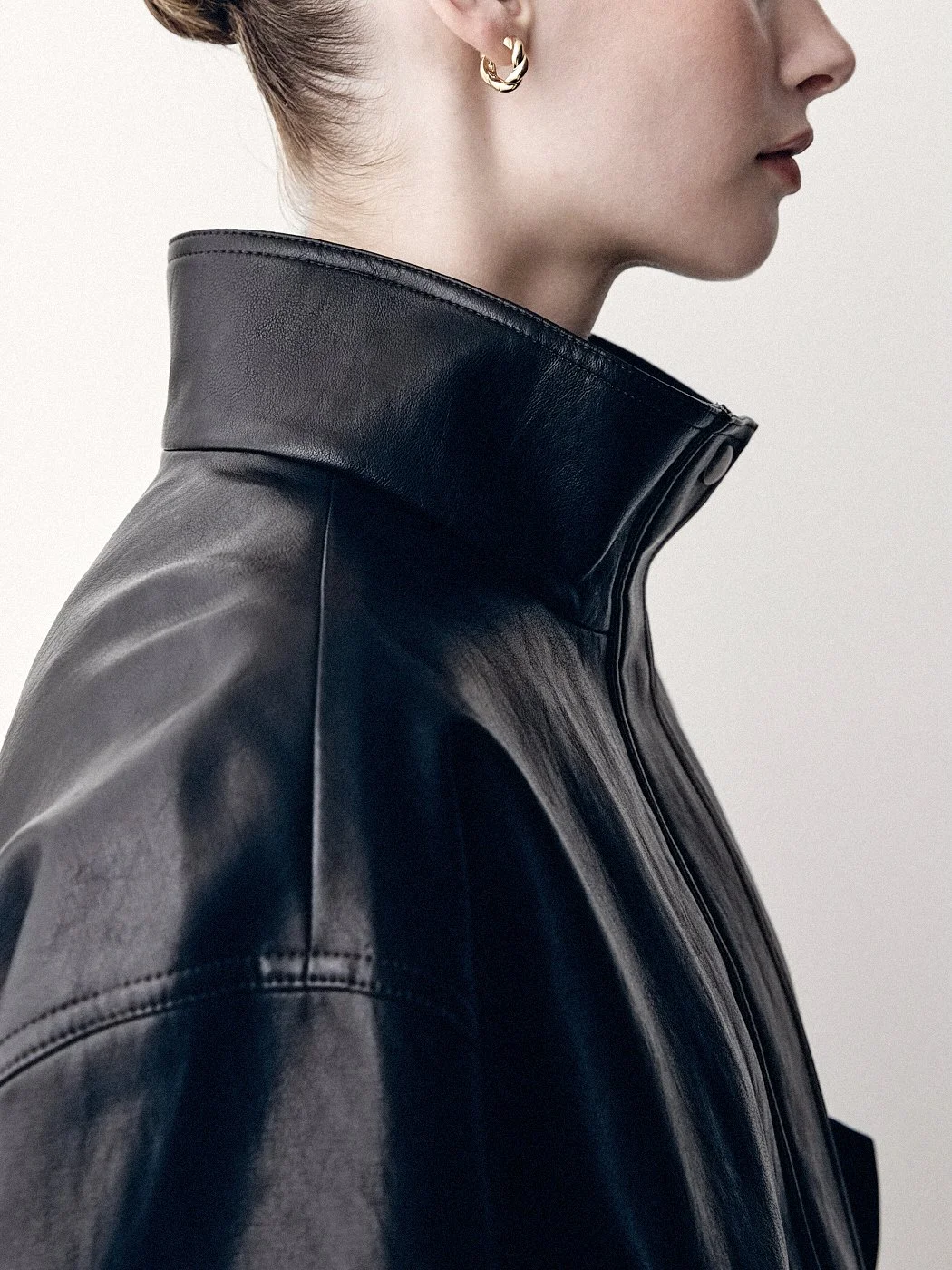 Close side view of a woman wearing a black leather jacket with a raised collar and gold hoop earring.