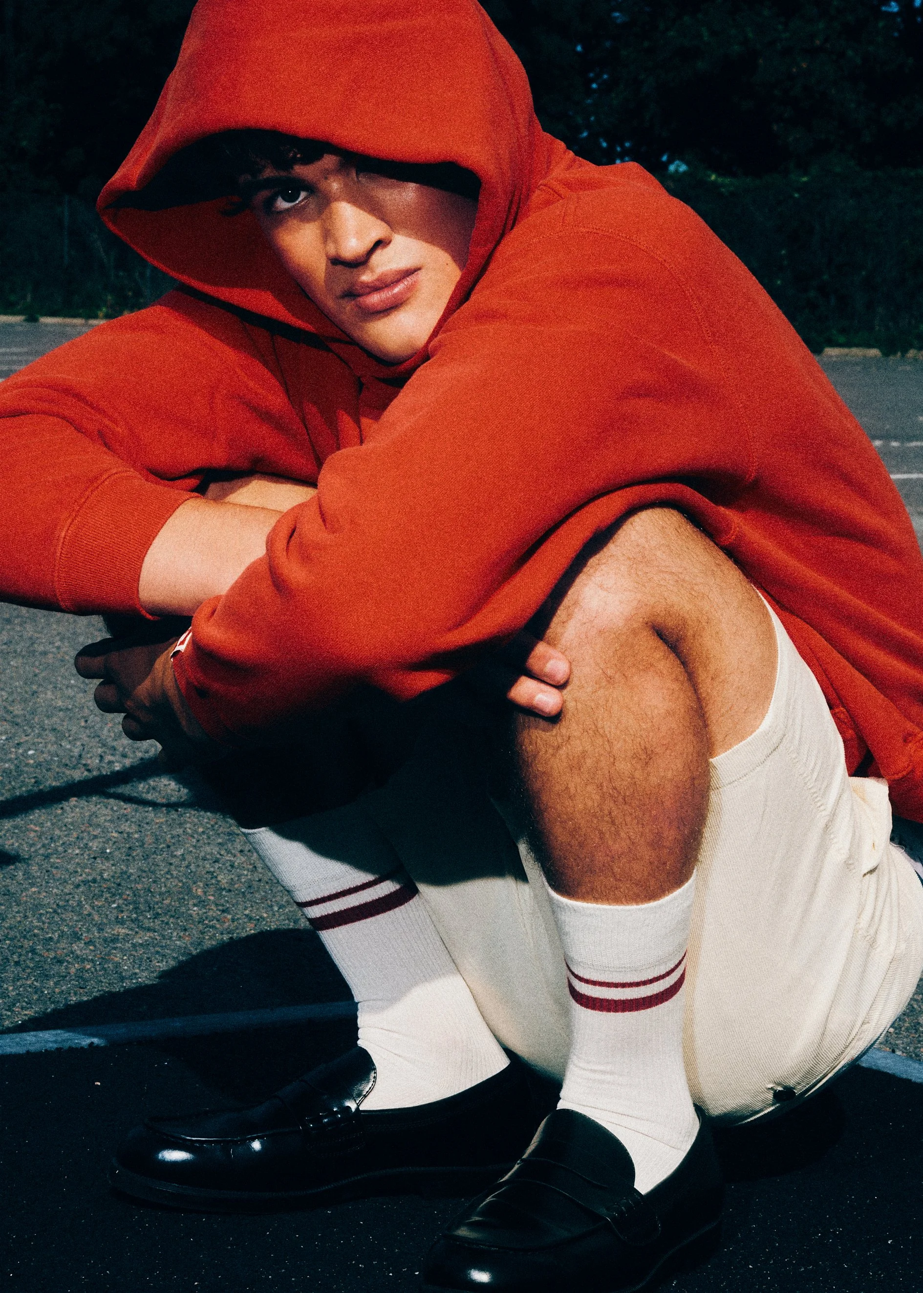 Man in a red hoodie and white shorts crouching on the ground. 