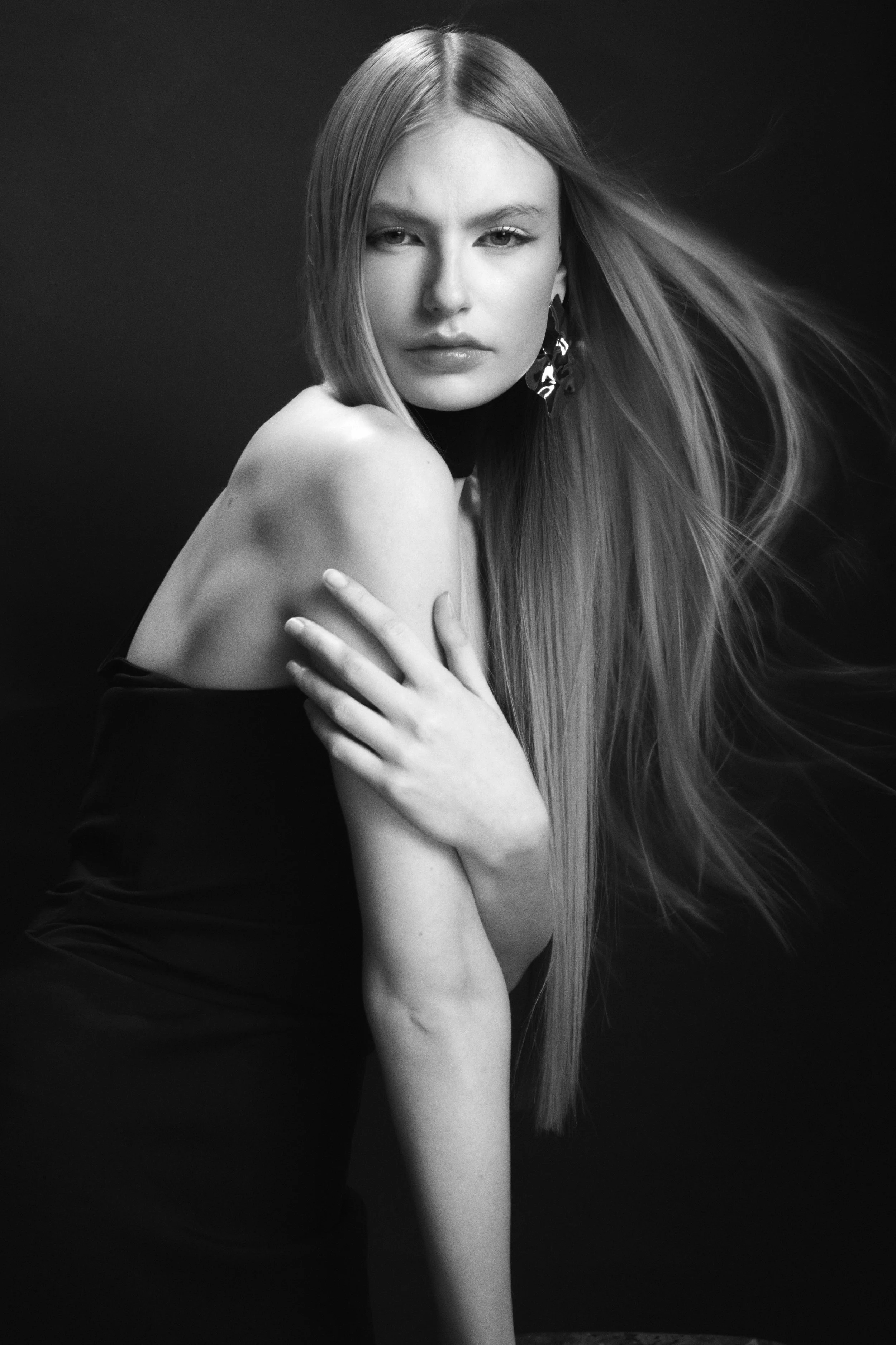 Black-and-white portrait of a woman with long straight hair holding one hand across her shoulder.