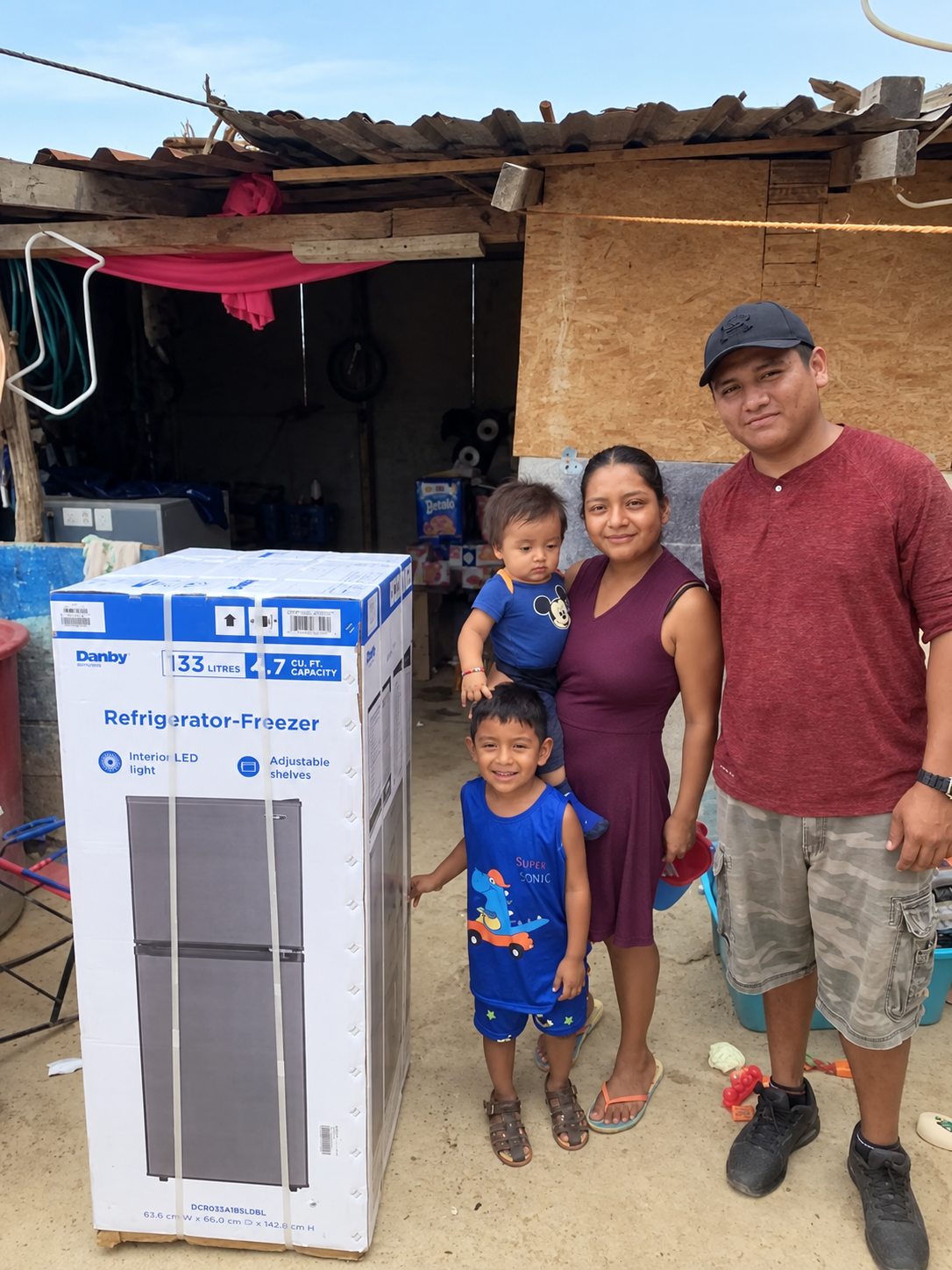 Ana and her family beside the boxed refrigerator provided by a donor.