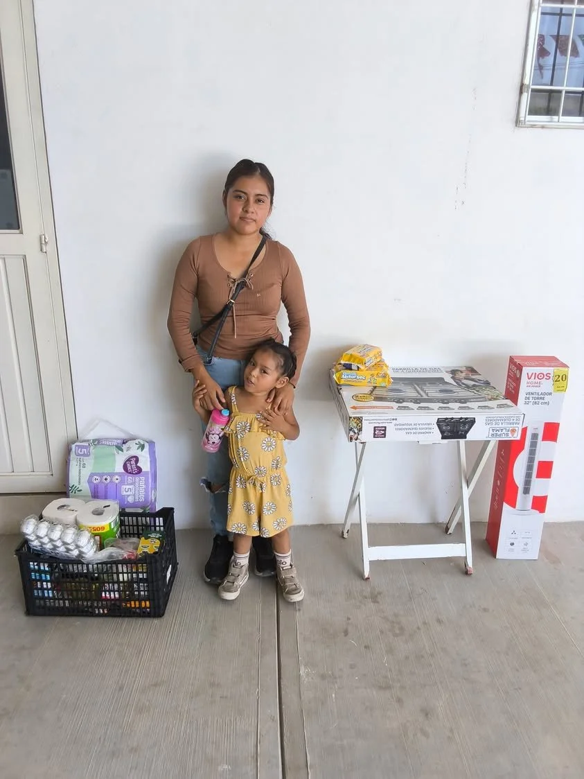 A mother and child beside groceries and household supplies received through family support.