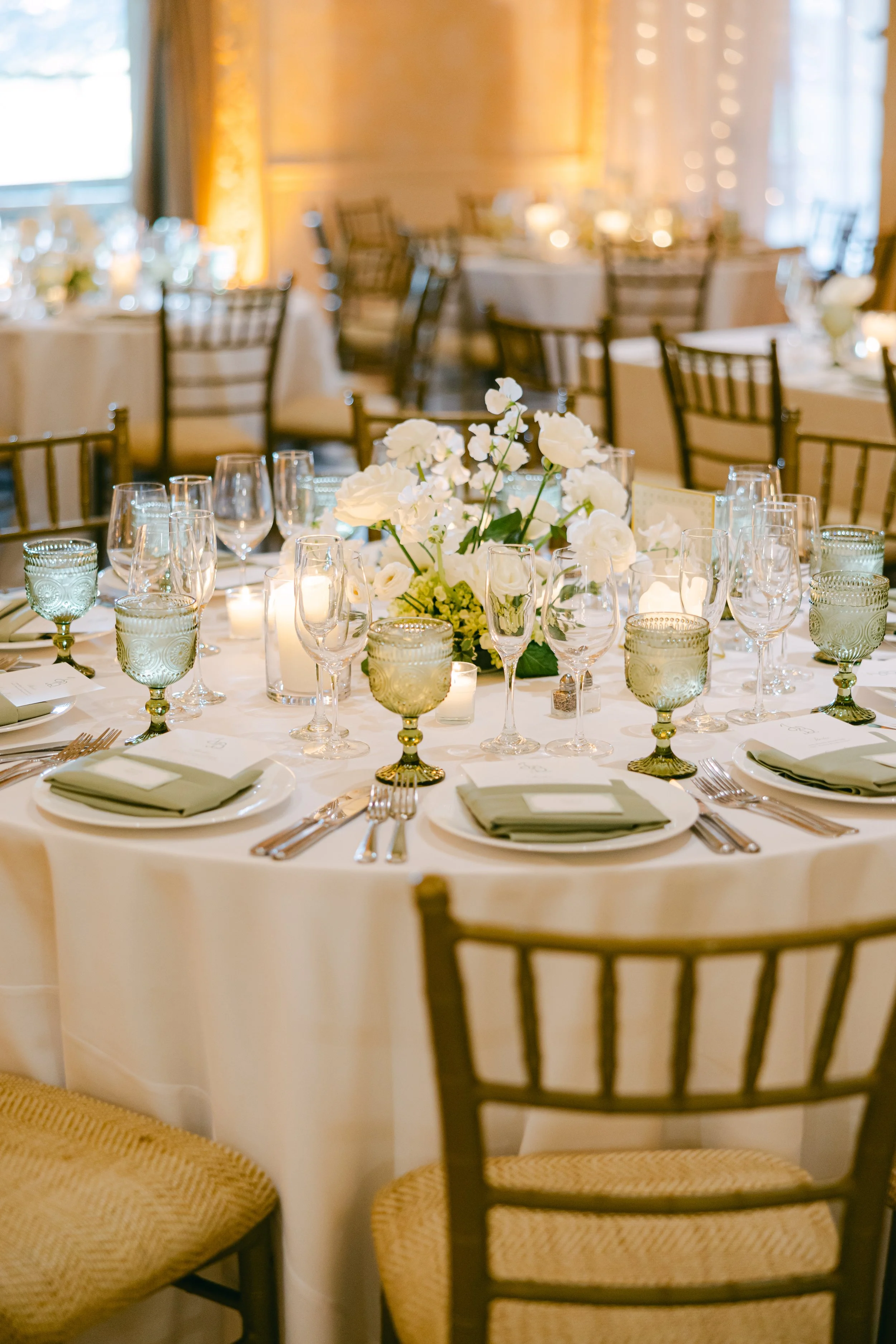 A round banquet table decorated with white flowers and candles, set for a formal event, with elegant chairs around it in a well-lit room.