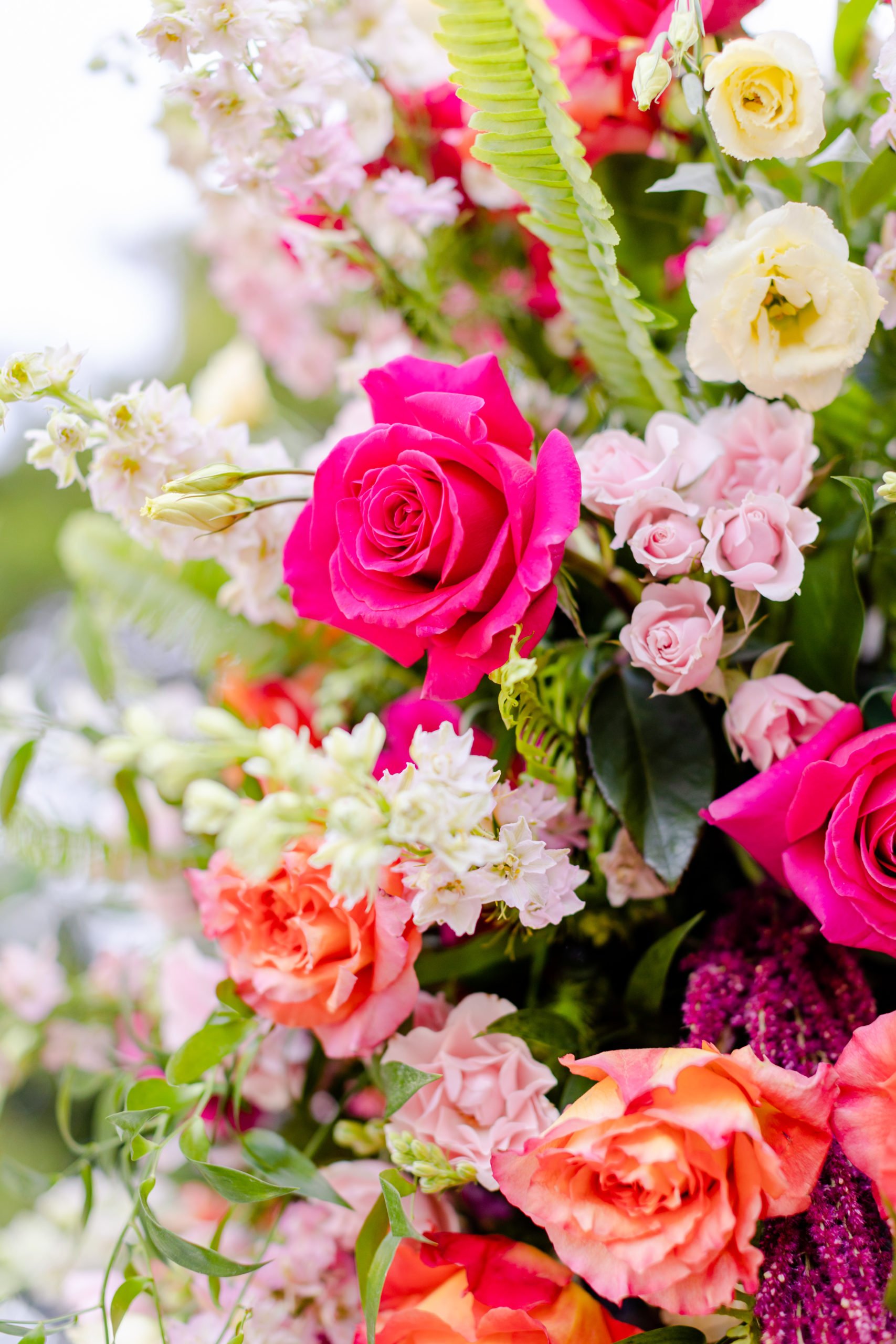 A vibrant bouquet of various pink, white, and purple flowers with green leaves and ferns.