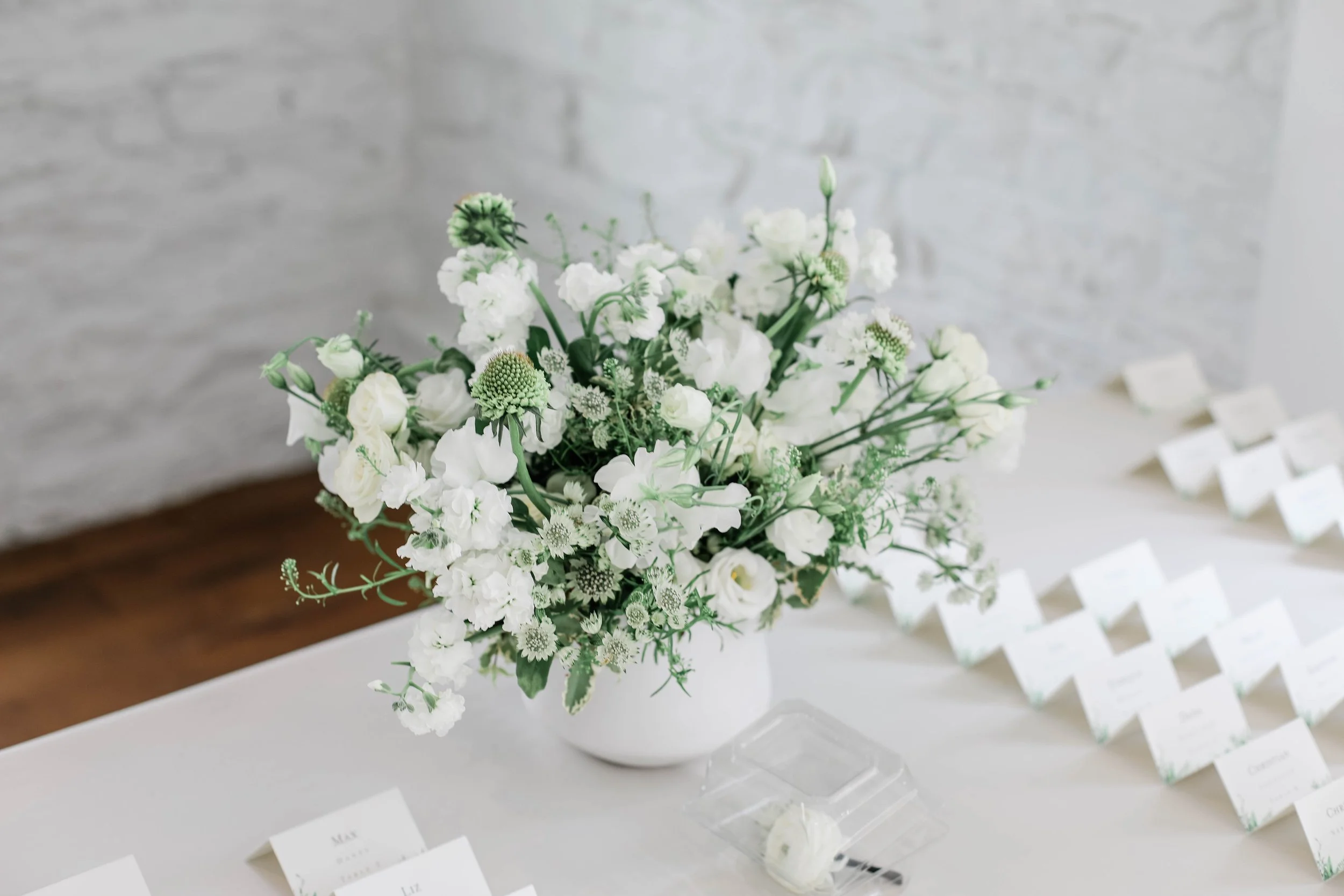 Placecard Table Arrangement in a white ceramic pot, matching white and green florals