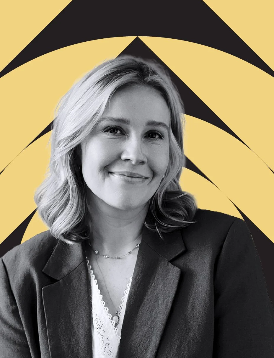 Black and white portrait of a smiling woman with shoulder-length blonde hair in business attire, set against a background featuring bold yellow and black geometric patterns.