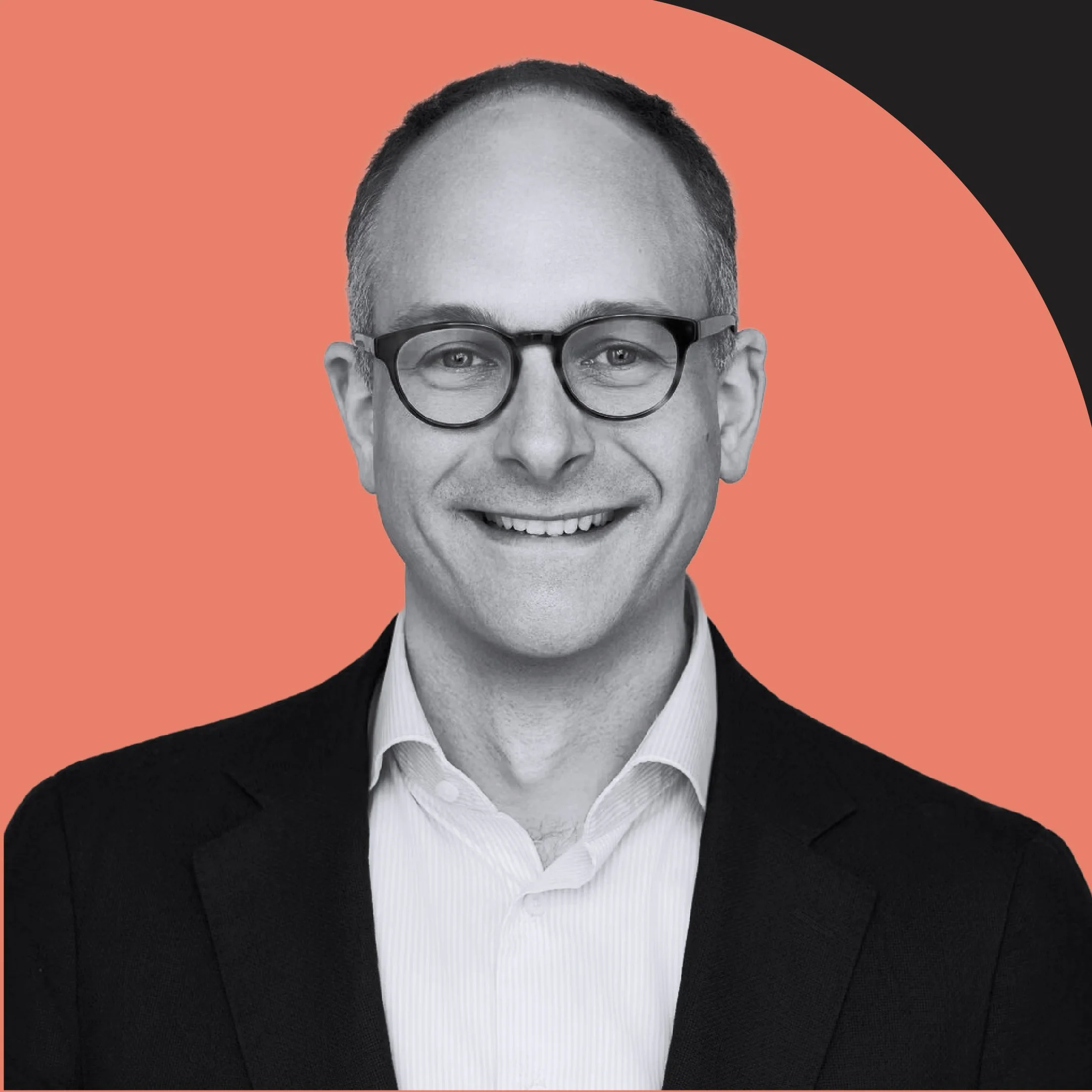Close-up black-and-white photo of a smiling man in a suit, white shirt, and round glasses with a patterned background of coral, black, and white.