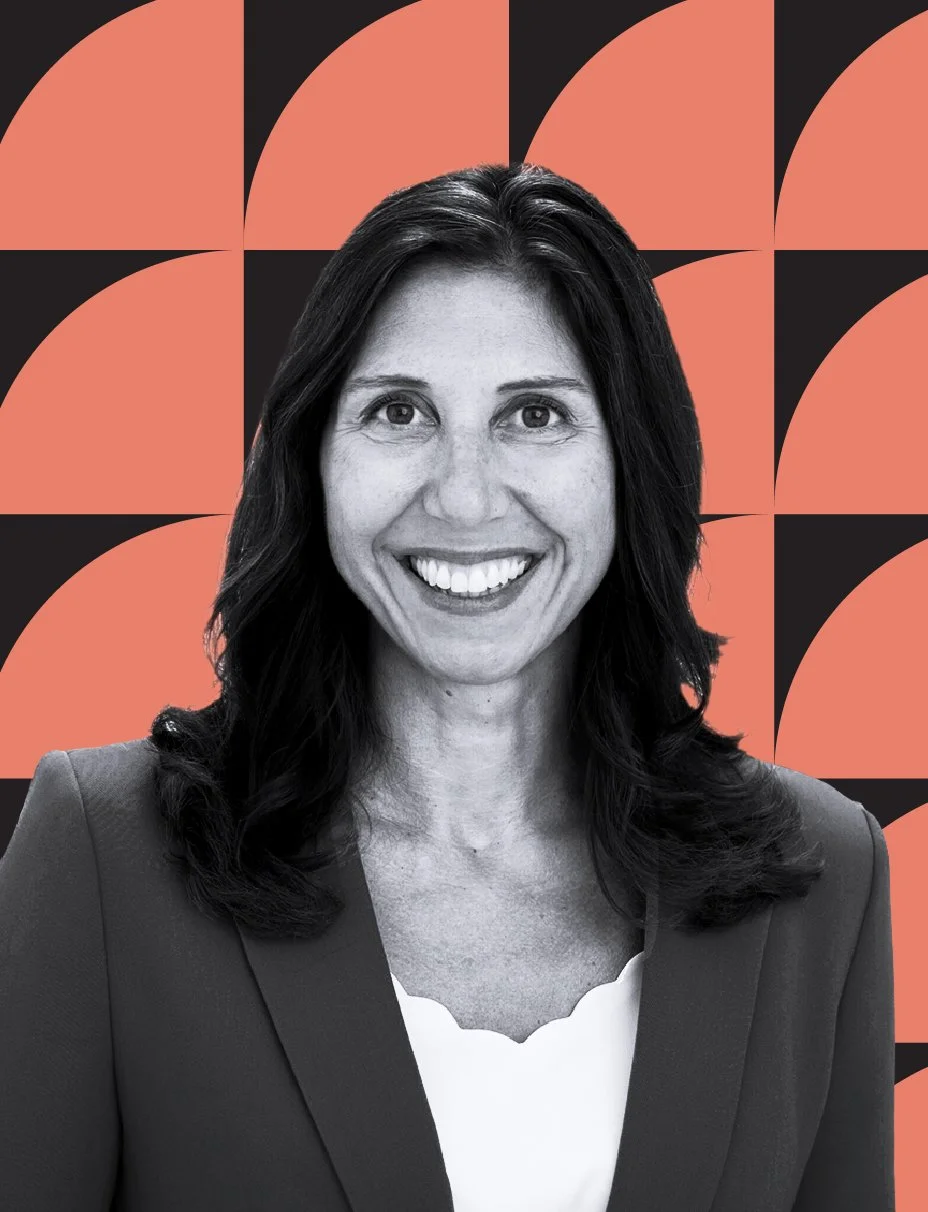 A black and white photo of a smiling woman with dark hair, wearing a blazer and white top, set against a geometric, coral and black patterned background.
