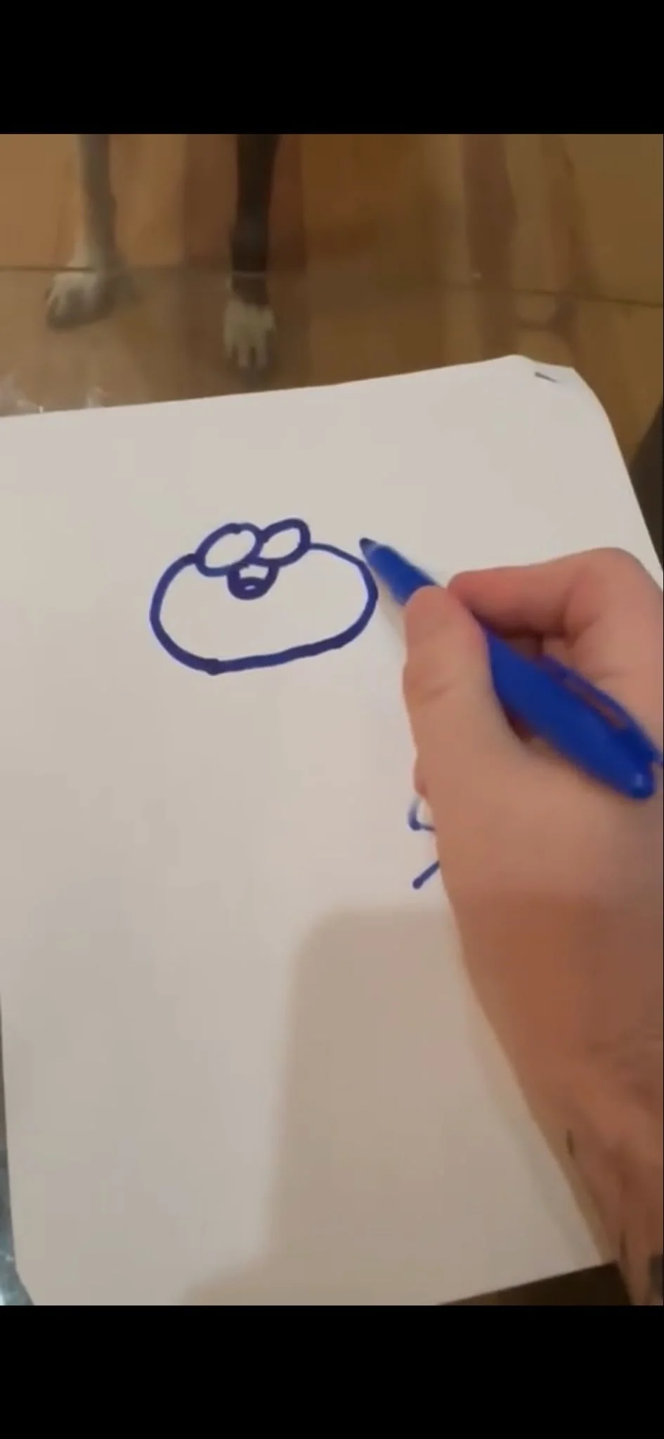 Drawing of a simple cartoon face with glasses on a white sheet of paper, held by a person using a blue marker.