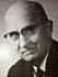 Black and white photo of a man with glasses, wearing a suit and tie.