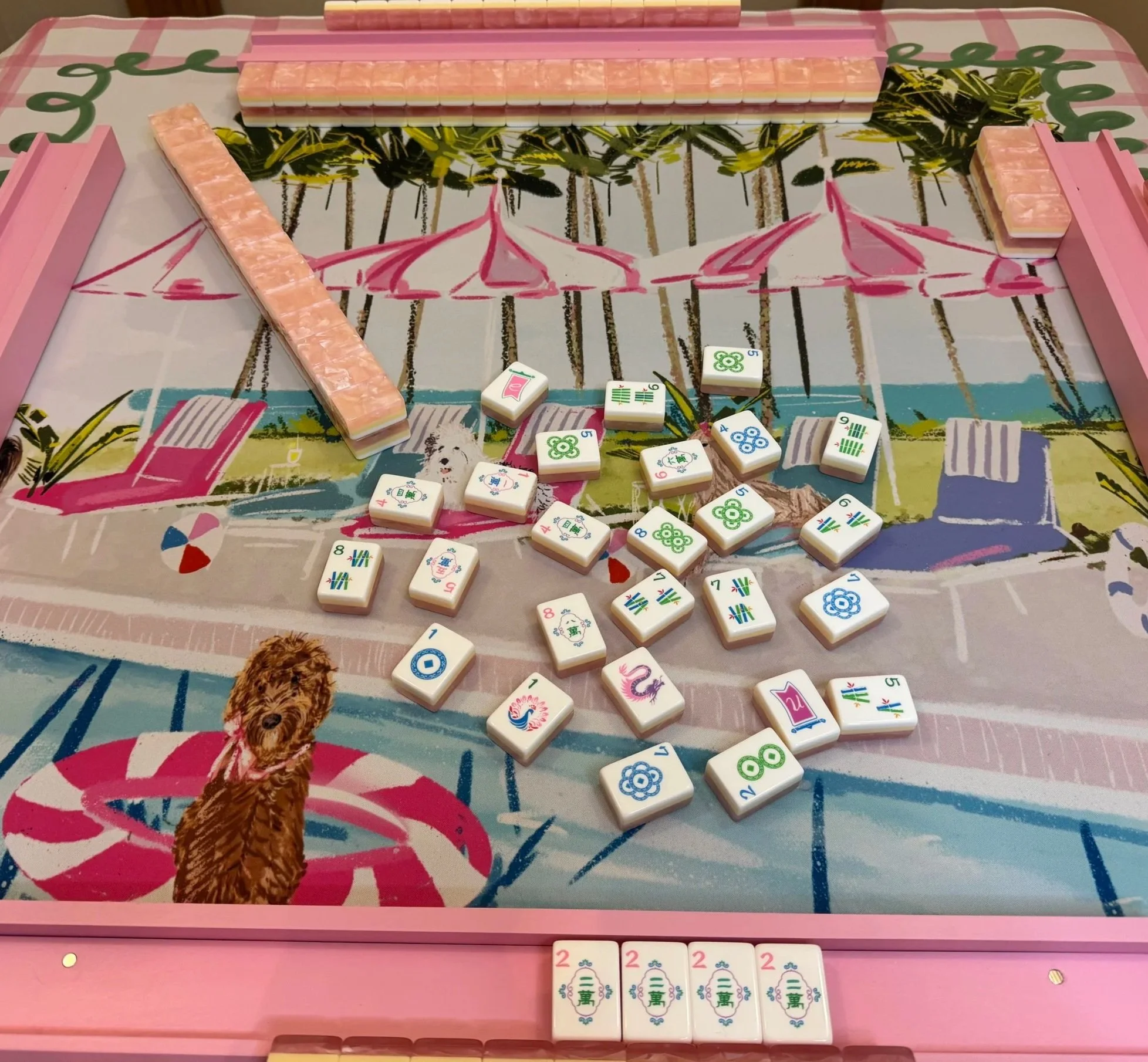 A pink Mahjong game table with tiles arranged on it, with a dog illustration and a dog figure on the table. Some Mahjong tiles are scattered in the foreground.