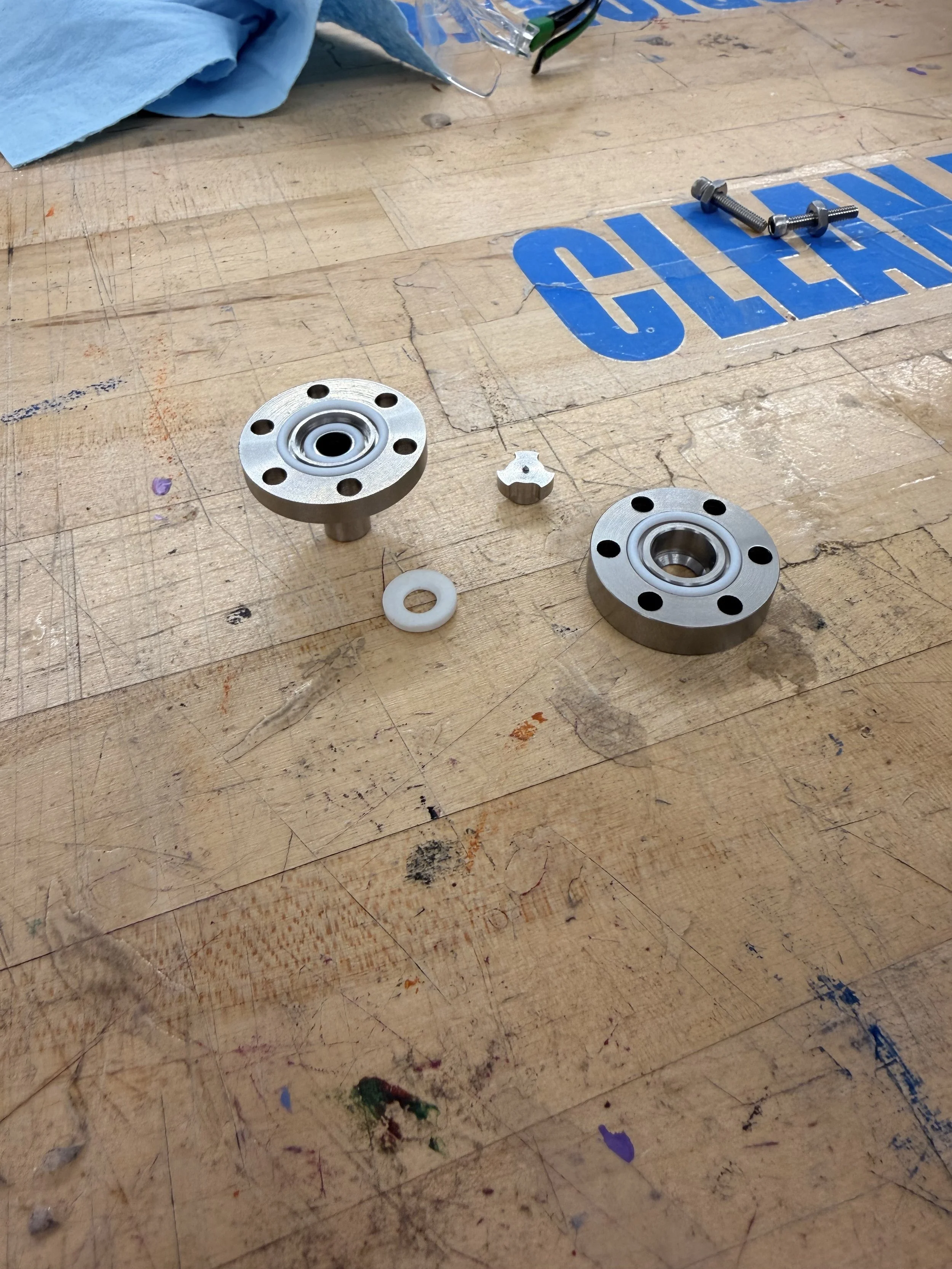 A wooden work surface with metal mechanical components, screws, washers, a blue cloth, and some signage painted on the wood.