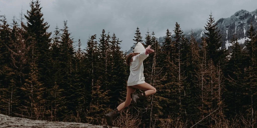 Child jumping in front of a forested mountain landscape