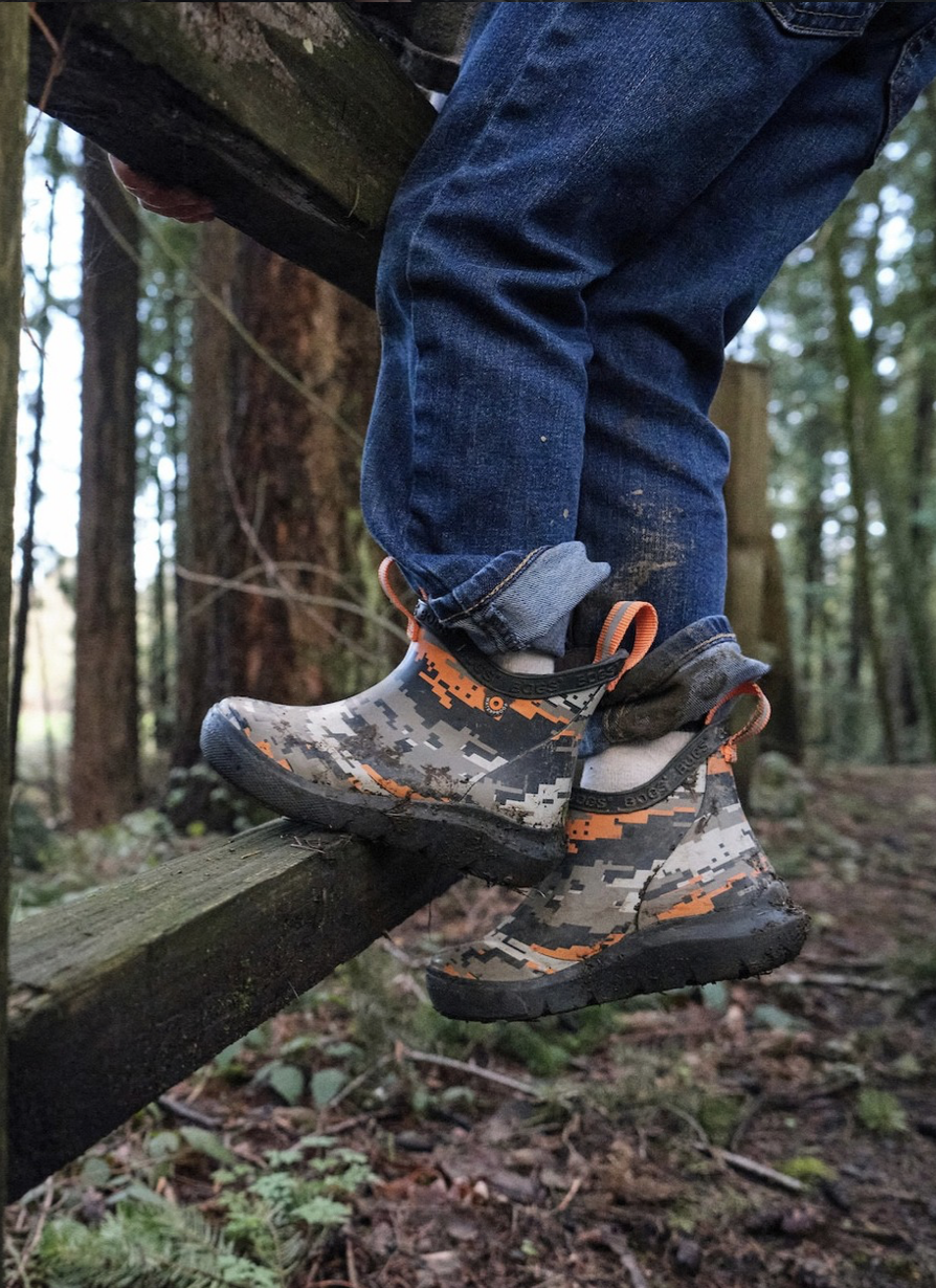 Person crossing a wooden rail on a trail in a forest, wearing camouflage patterned waterproof boots and blue jeans.